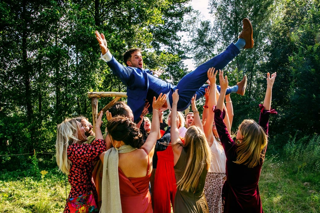 Een man in pak wordt tijdens een bruiloft door zijn groepsfotolijstvrienden de lucht in gegooid.