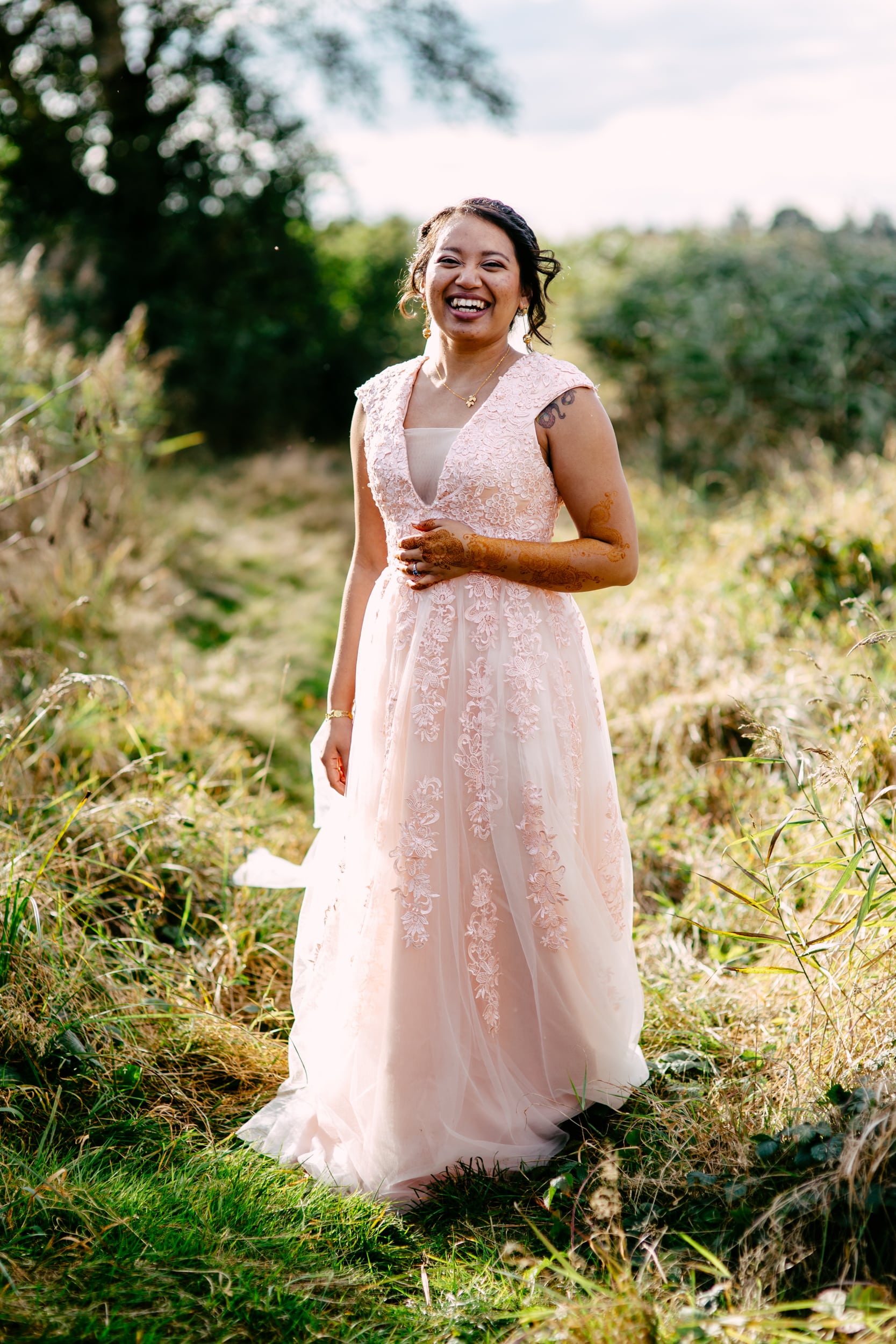 A Bohemian bride in a pink dress standing in a field.
