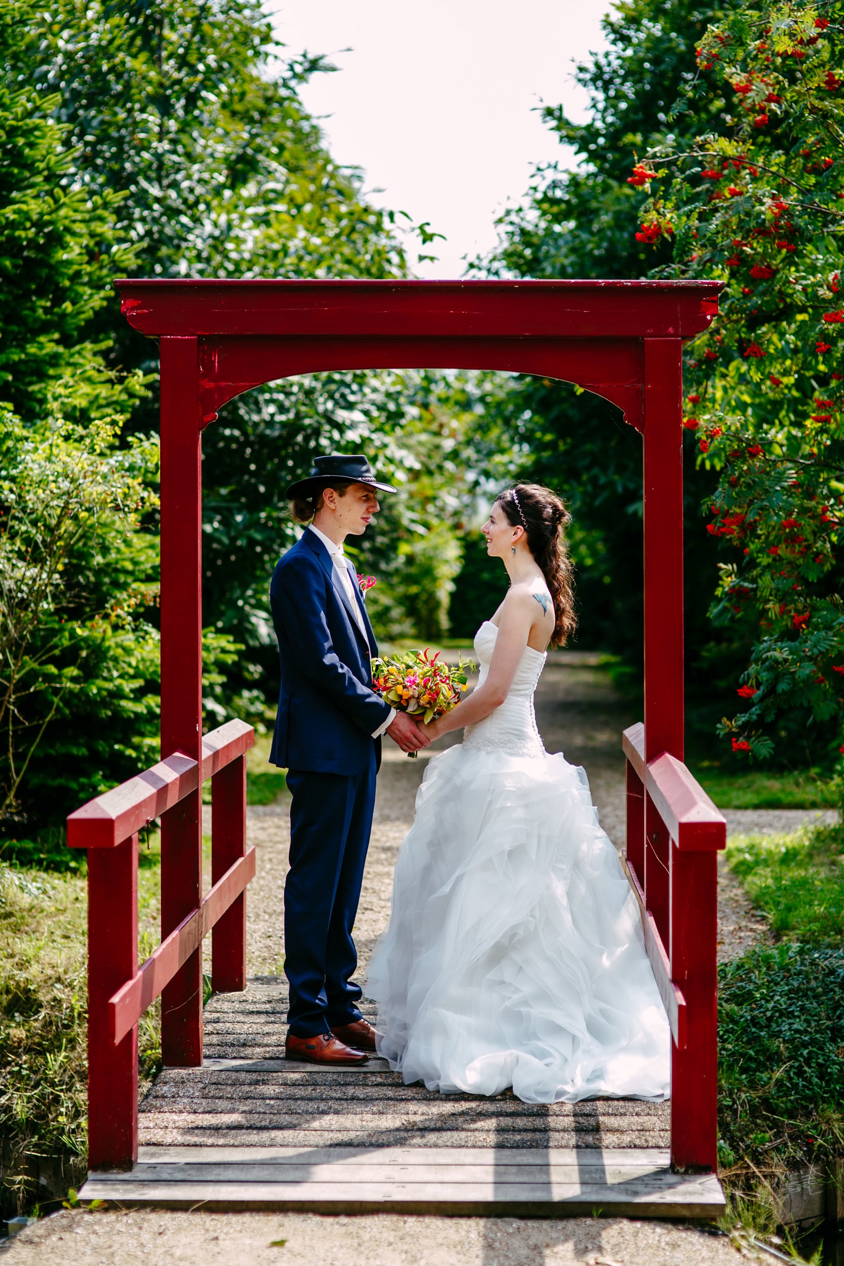 A budget bride and groom stand on a red bridge in a garden and enjoy their cheap wedding.