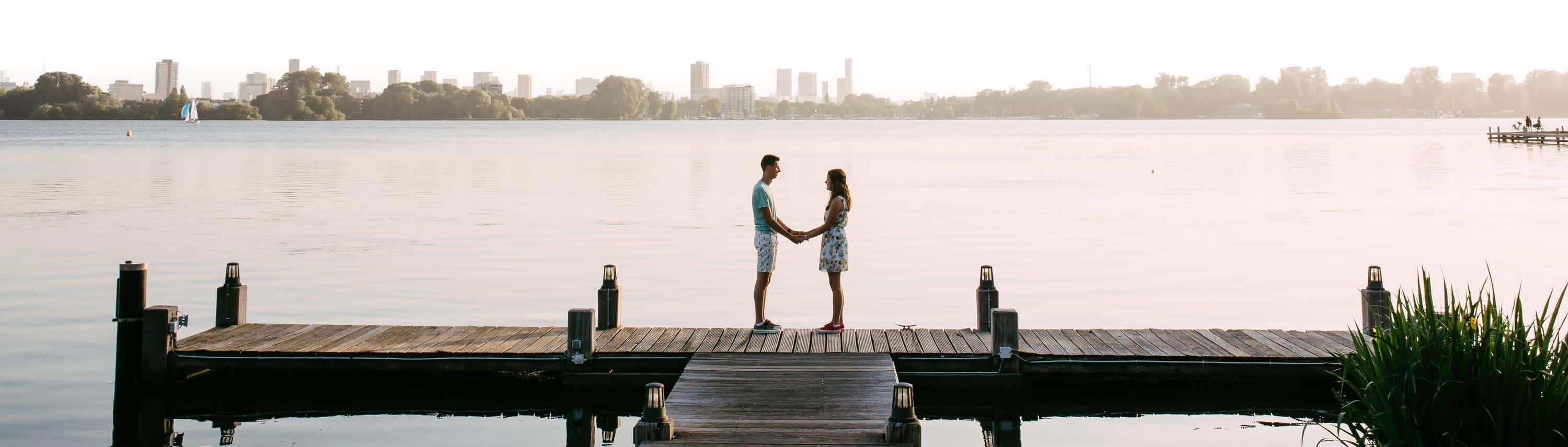 An affectionate couple standing on a quay overlooking a picturesque lake during their love shoot.