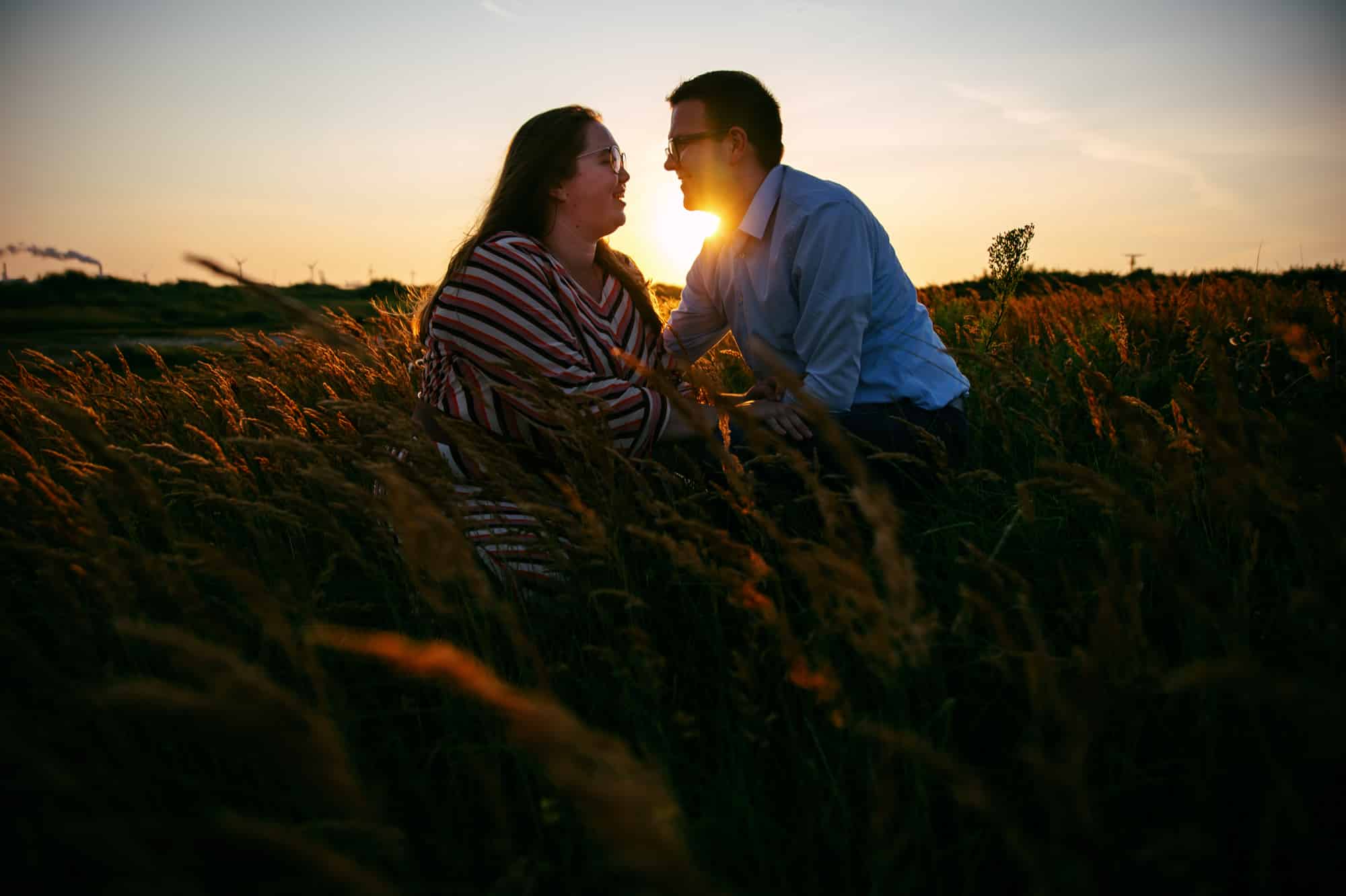 Loveshoot: een koppel dat hartstochtelijk kust in een veld bij zonsondergang.