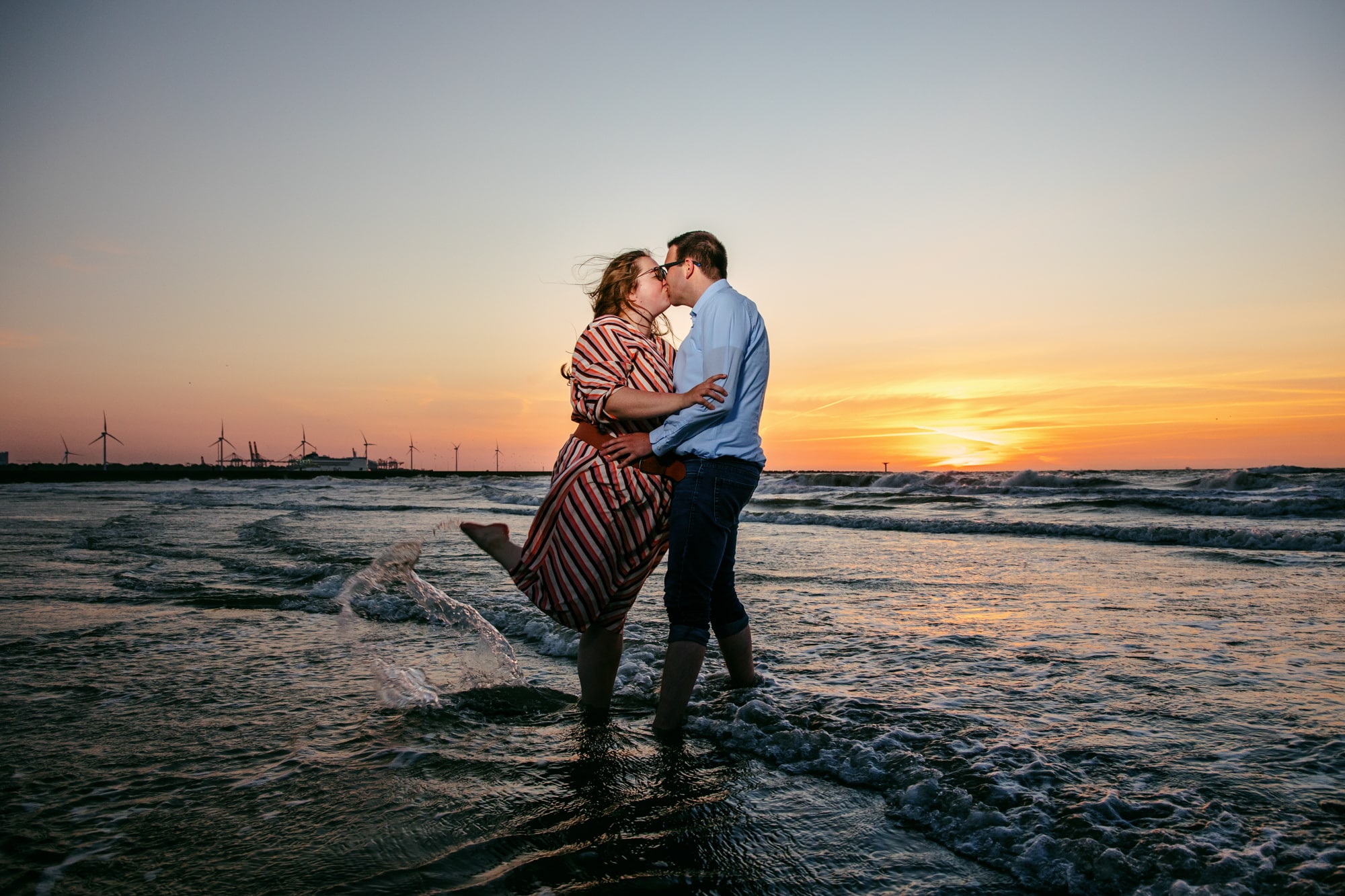 Een gepassioneerde loveshoot waarin een kussend koppel in de oceaan bij zonsondergang wordt vastgelegd.