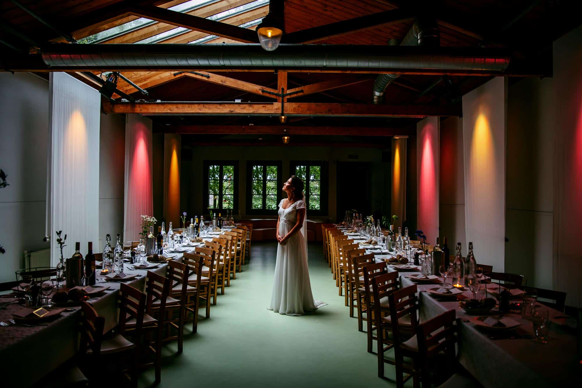 A bride standing in the middle of a room with tables and chairs.