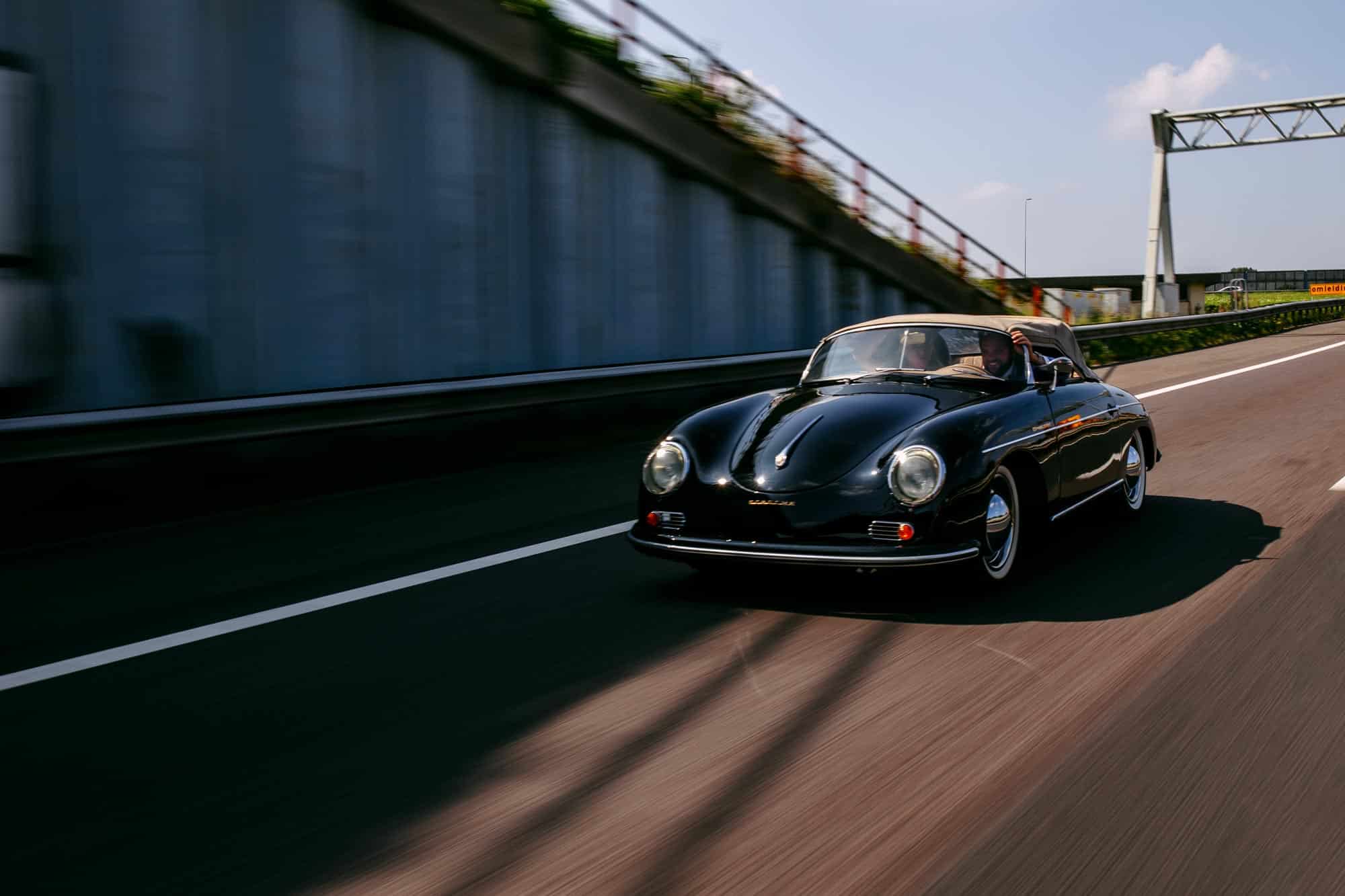 Een zwarte Porsche 356 speedster die over de snelweg rijdt en bijzondere trouwfoto's maakt.