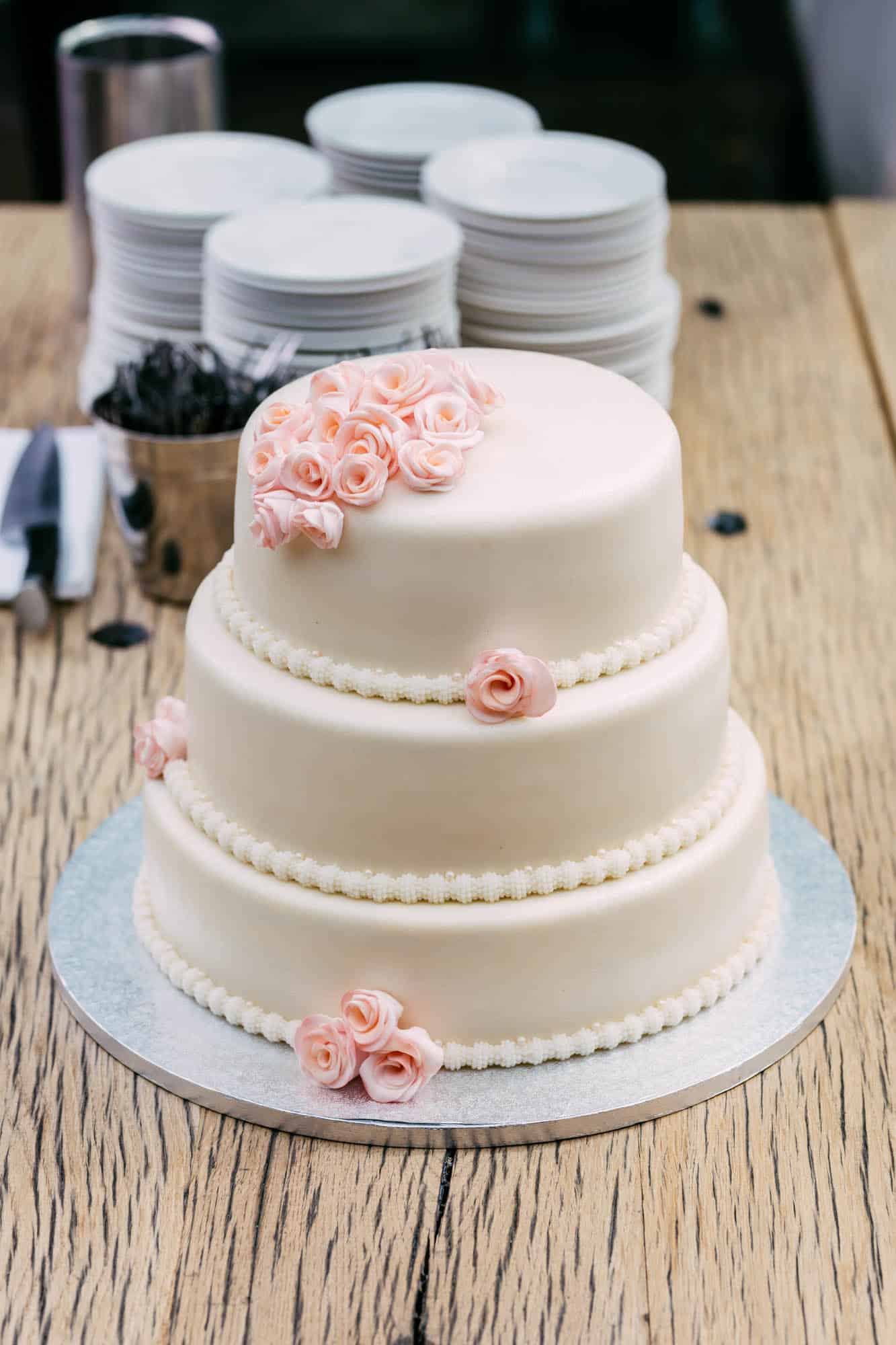 A white wedding cake decorated with pink roses on top.