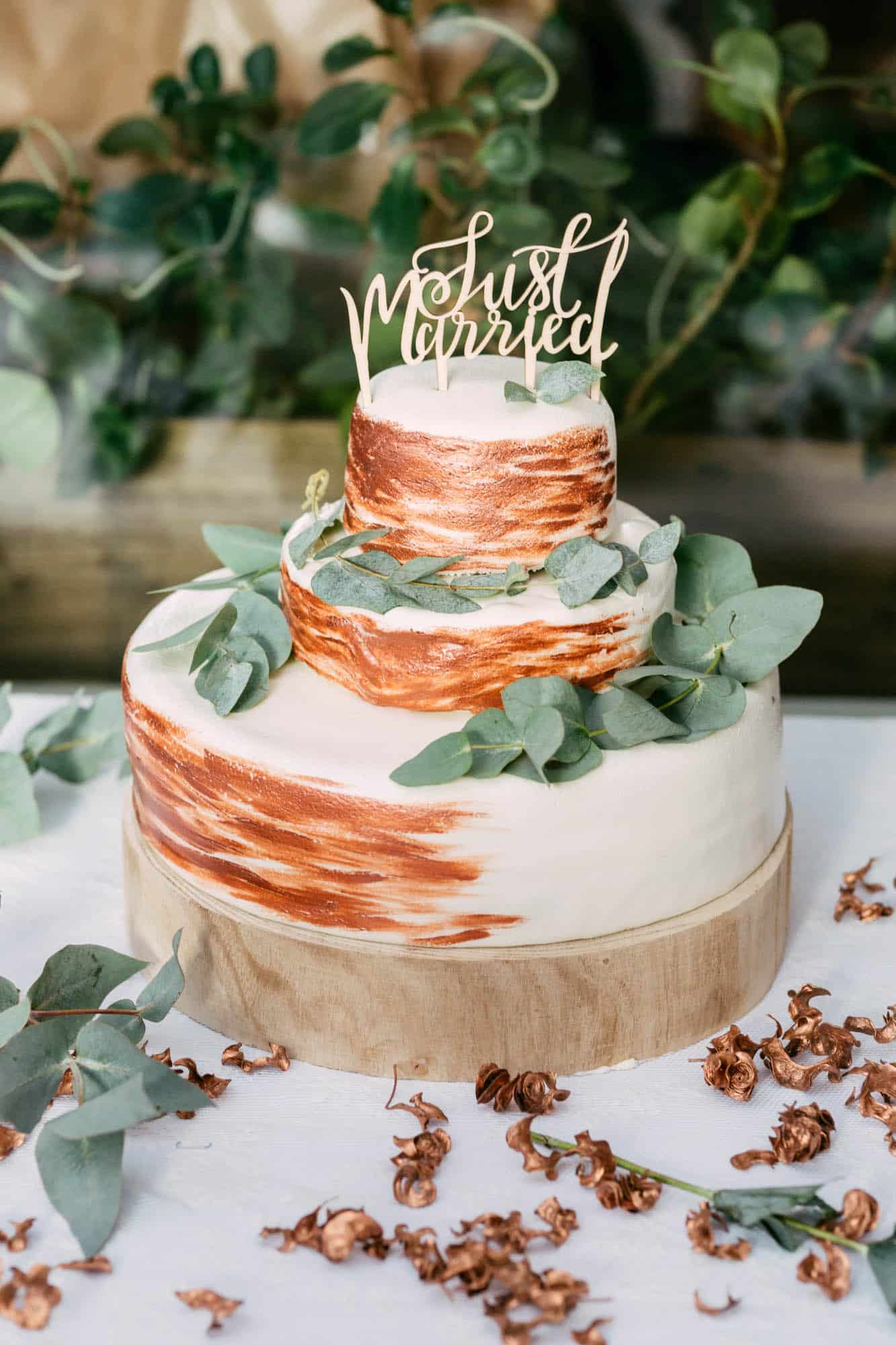 A wedding cake with eucalyptus leaves above it.