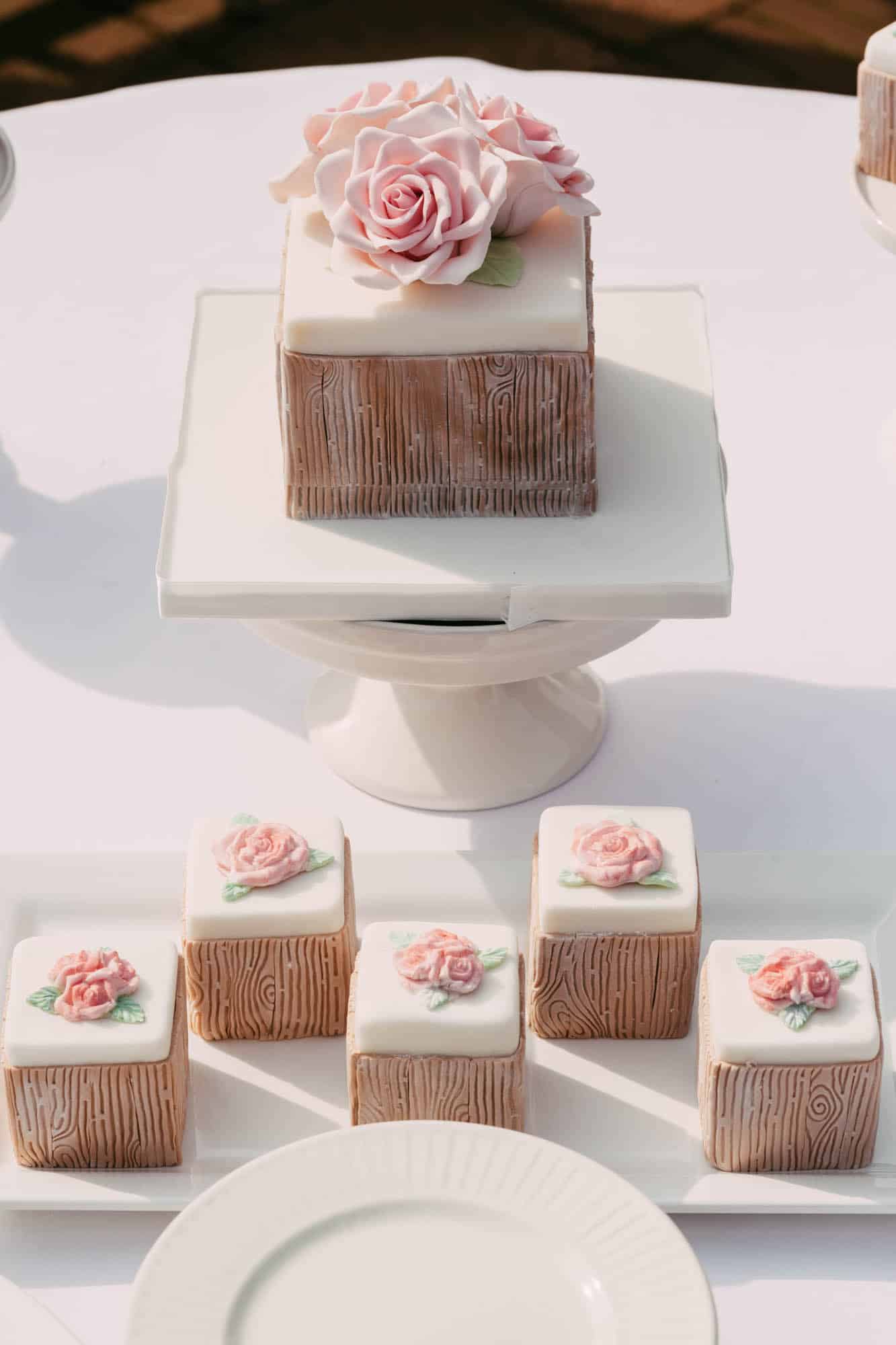 A white cake with pink roses on a white plate, perfect for wedding cakes.