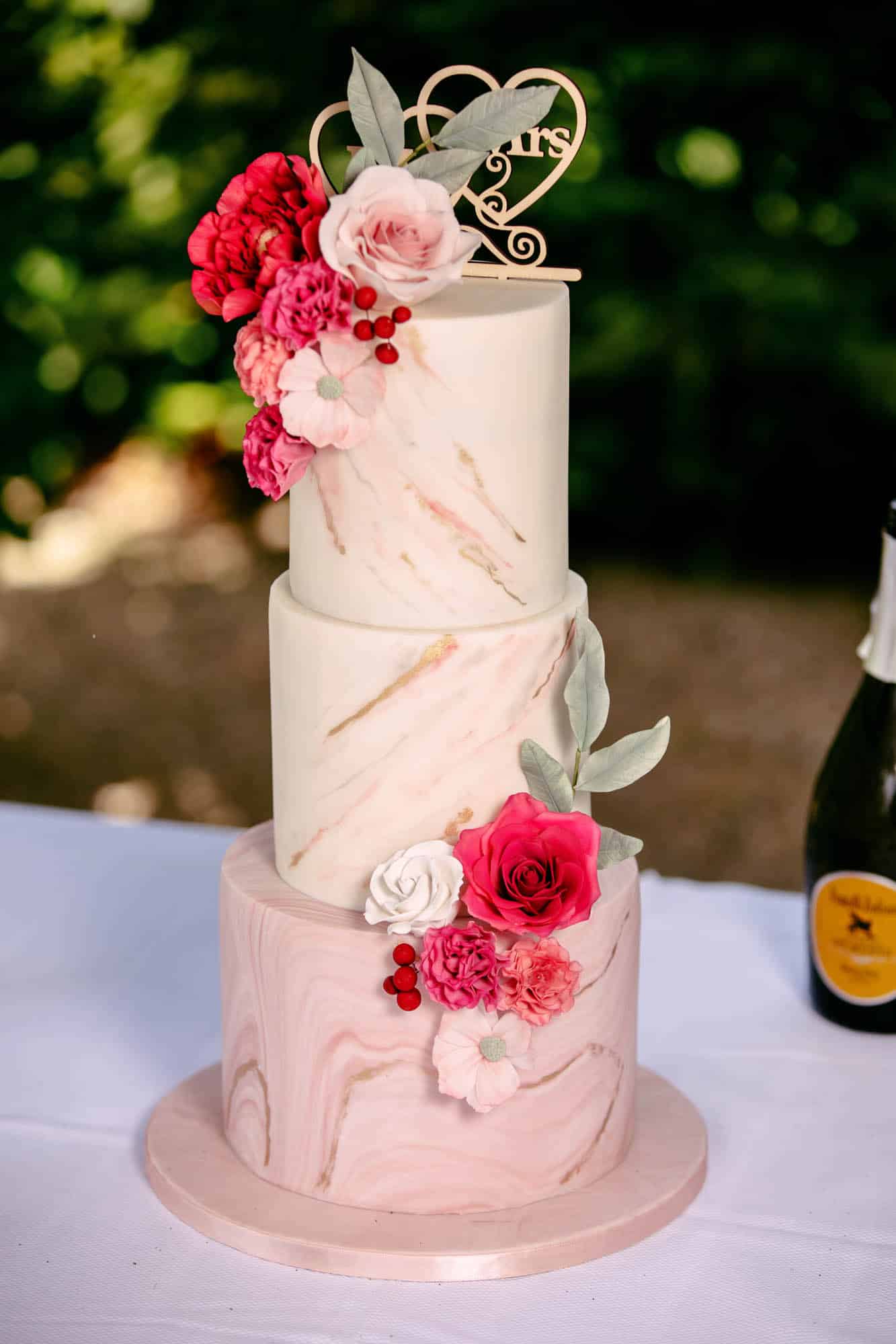 A beautifully decorated wedding cake with three layers and pink flowers on top, perfect for wedding cakes.