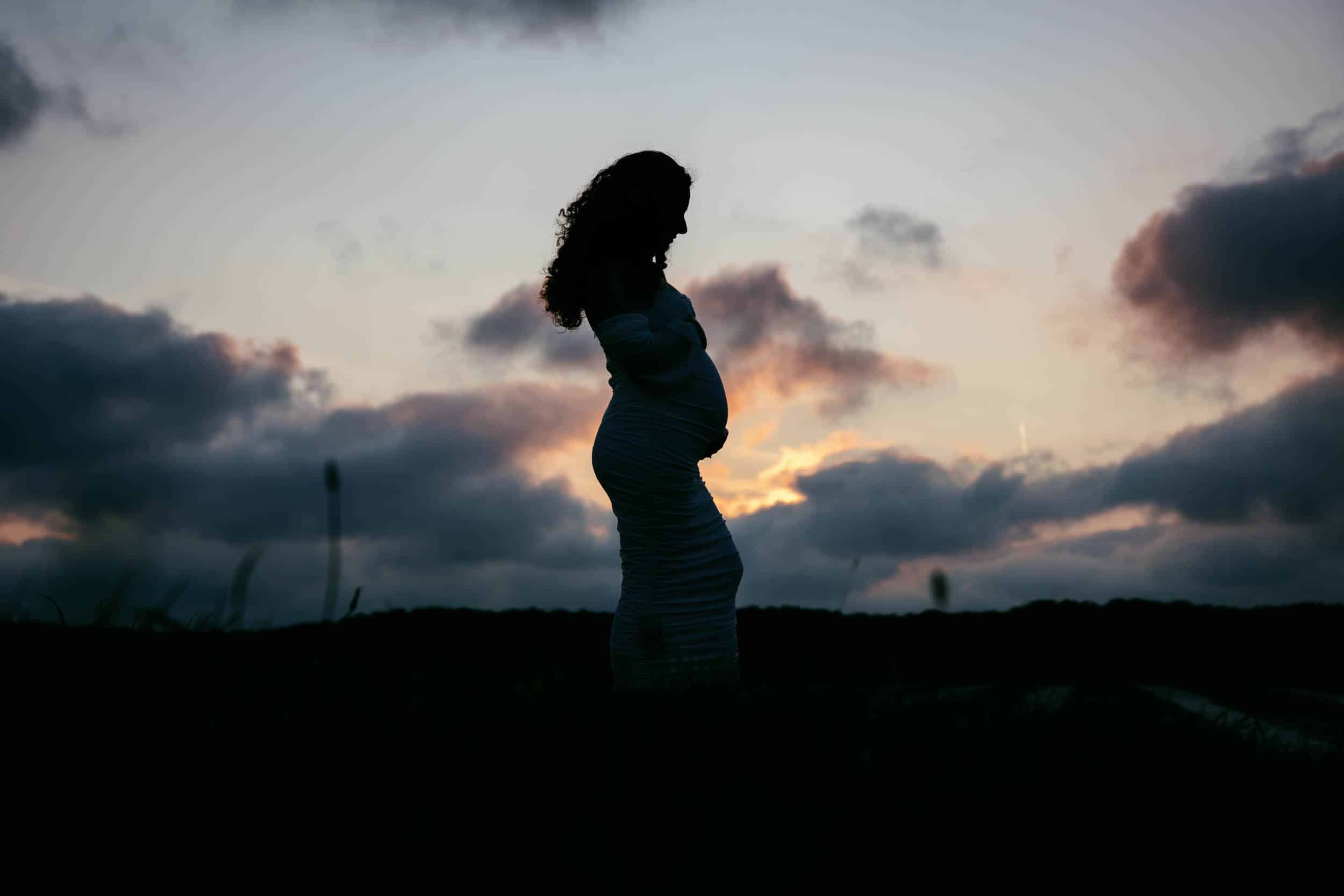 Een prachtige zwangerschapsshoot waarin het silhouet wordt vastgelegd van een zwangere vrouw die bij zonsondergang in een veld staat.