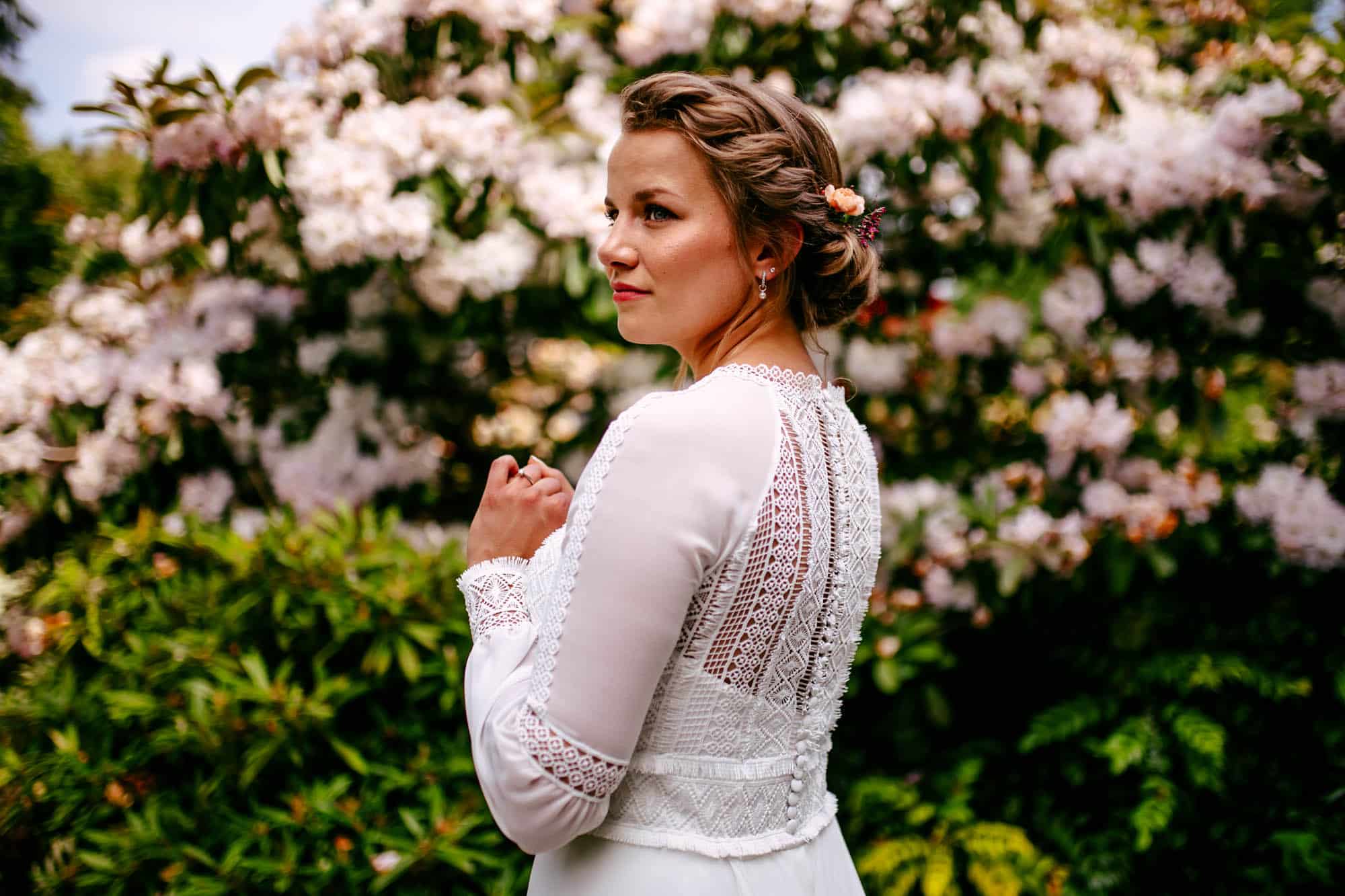 A Bohemian bride in a white dress standing in front of flowers.
