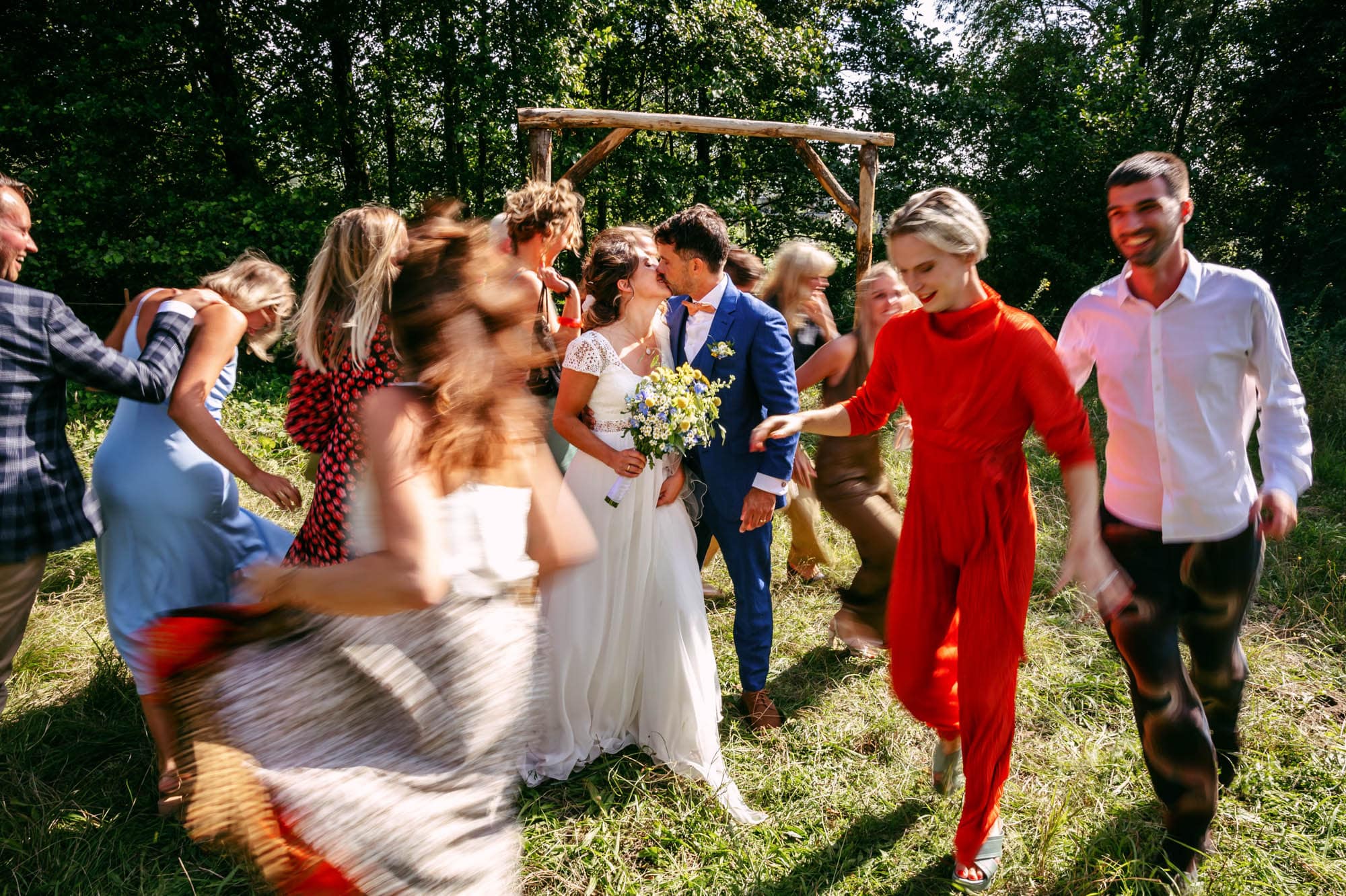 A group of Bohemian brides and grooms dancing in the forest, in beautiful wedding dresses.