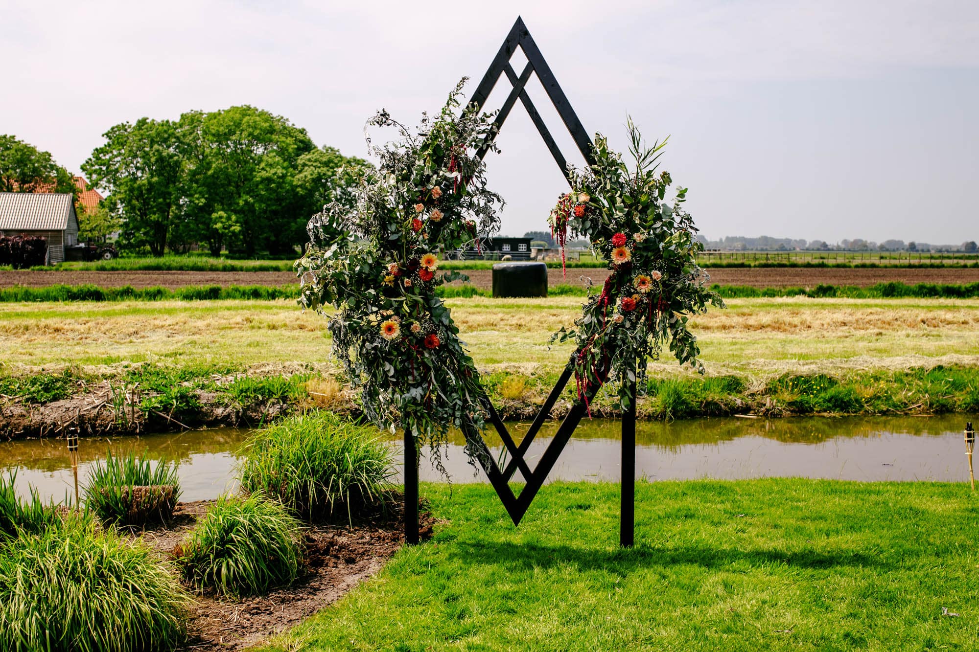 Een huwelijksboog met bloemen en een vijver op de achtergrond.