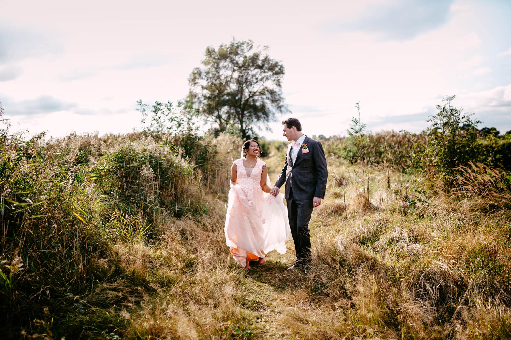 A Bohemian bride and groom walking through tall grass in a field, exuding effortless style.