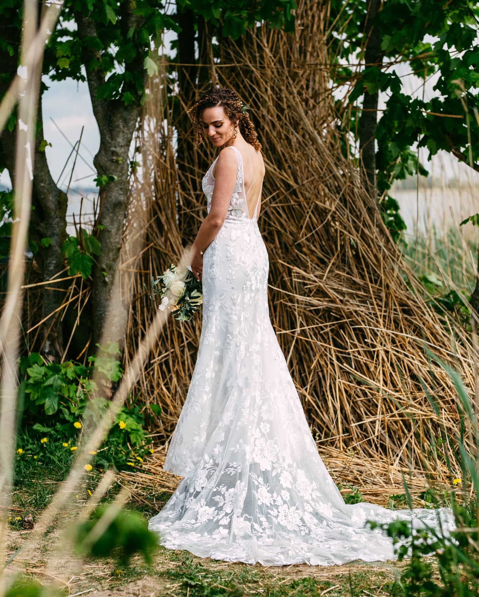 A Bohemian bride in a lace wedding dress standing in the grass.
