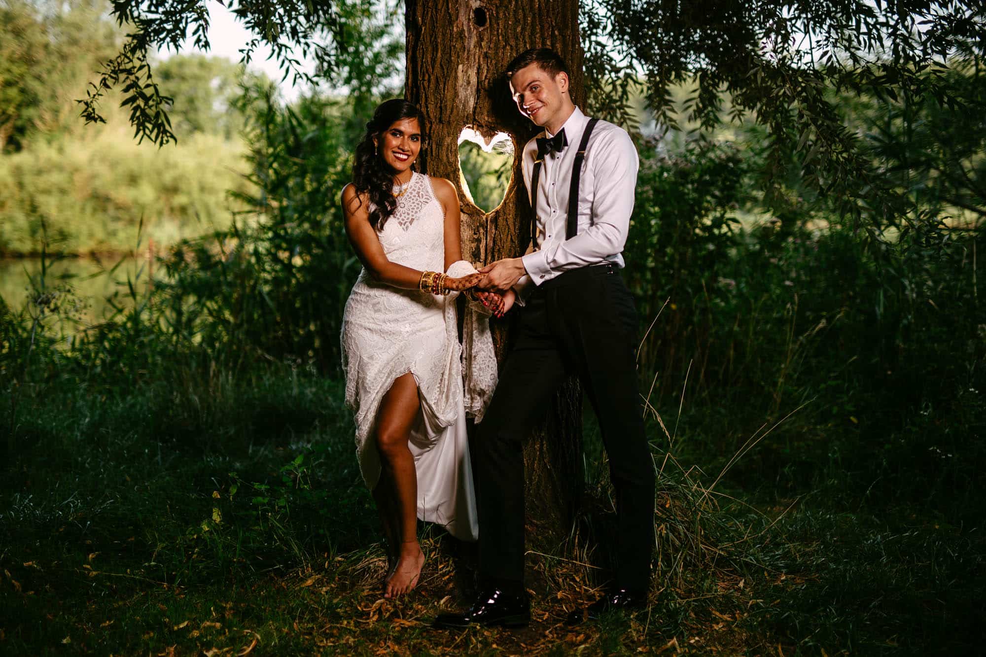 A bohemian bride and groom stand next to a tree, adorned in a beautiful wedding dress.