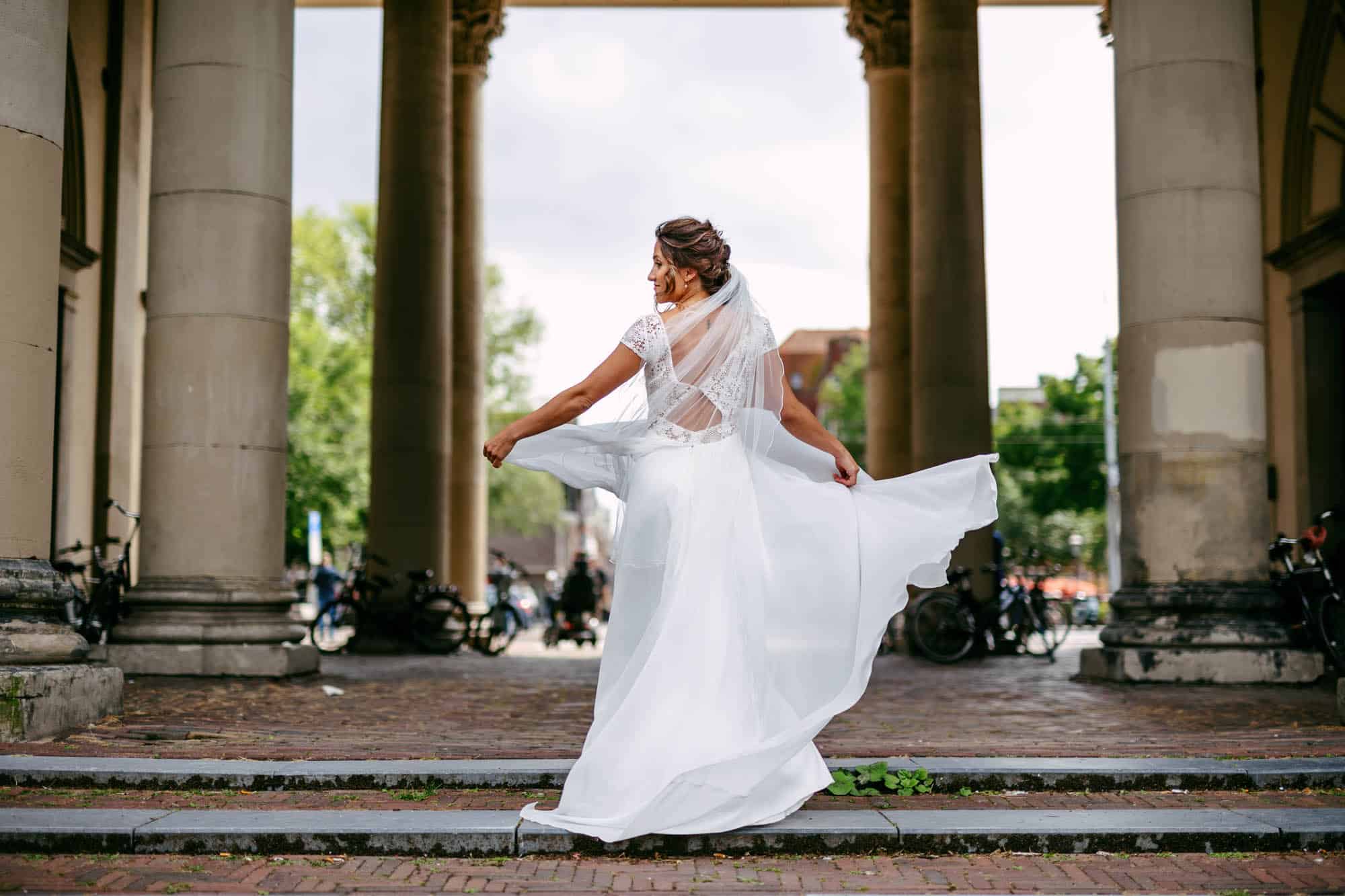 A Bohemian bride in a white dress walks down the steps of an old building.