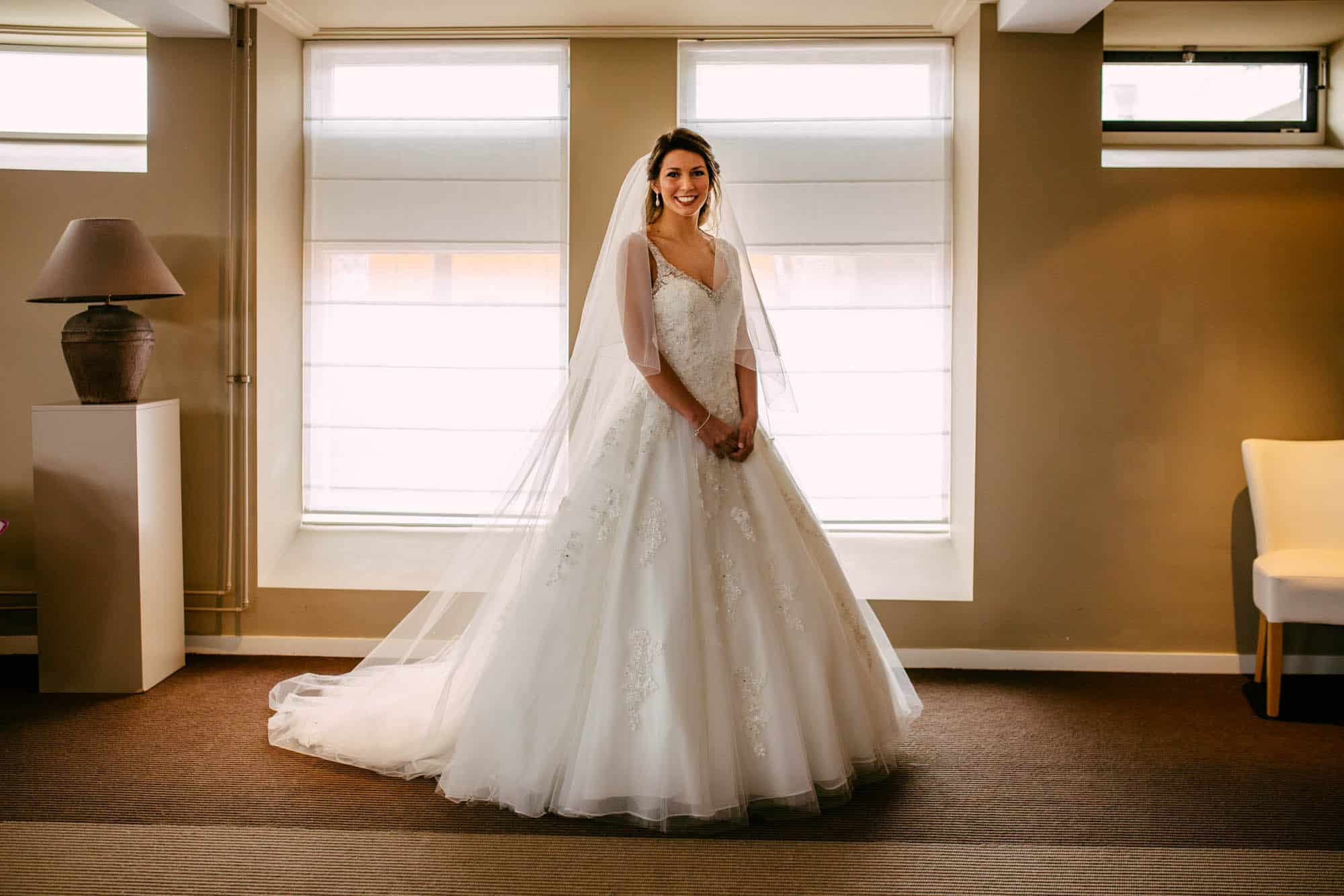 Beschrijving: Een bruid in een trouwjurk staat in een kamer.