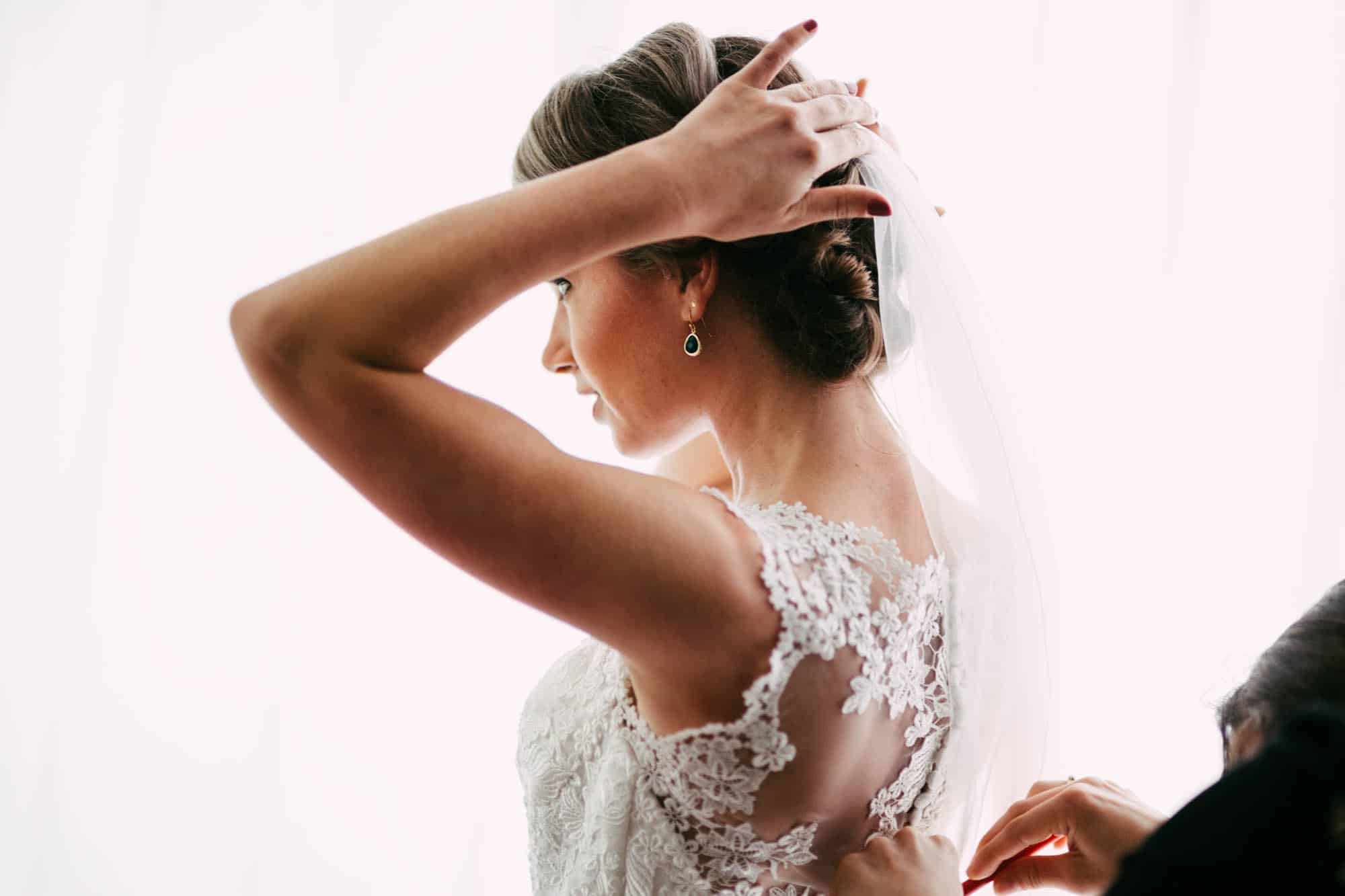 A bride wearing her wedding dress and putting on her bridal veil.