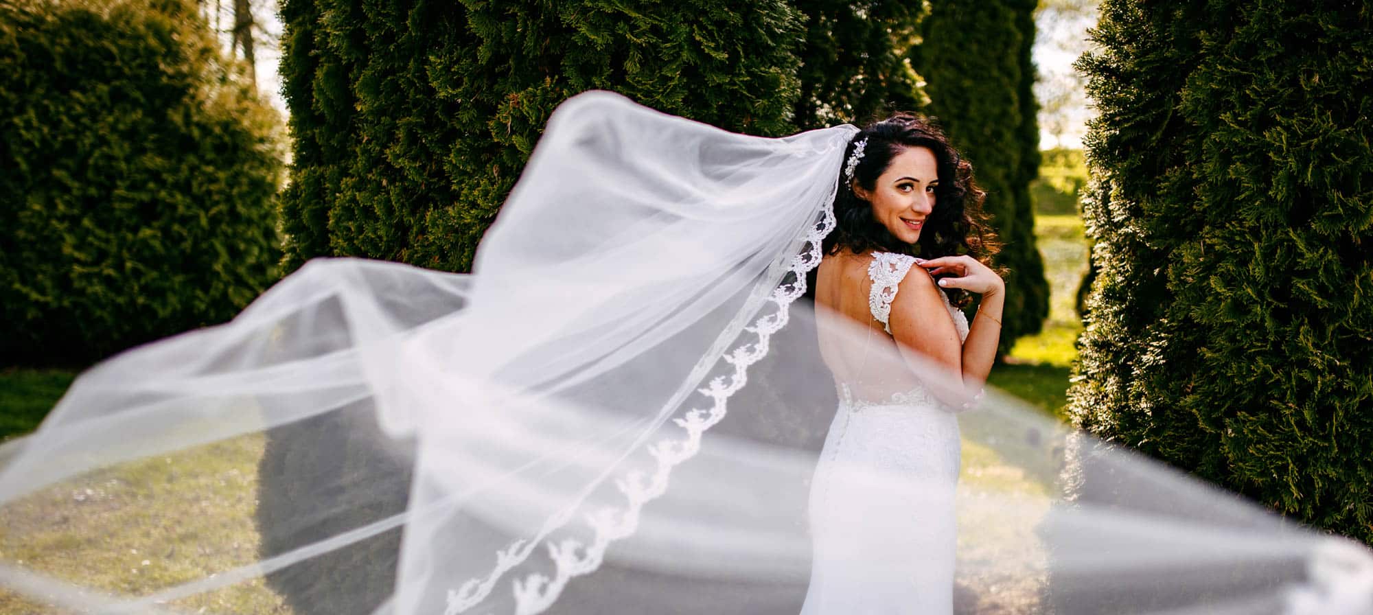 Een bruid in haar trouwjurk met haar sluier wapperend in de wind.