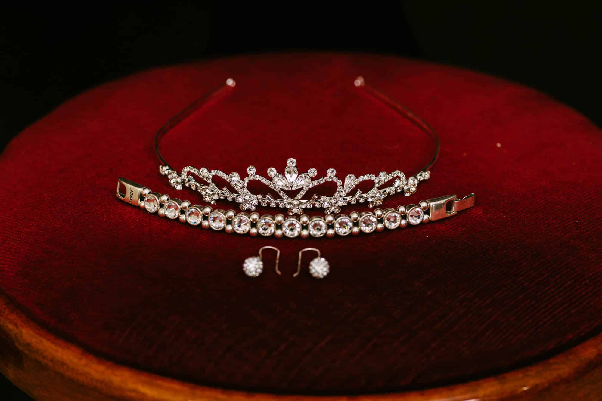 Een tiara en oorbellen op een rode tafel, perfect voor bruidskapsels.