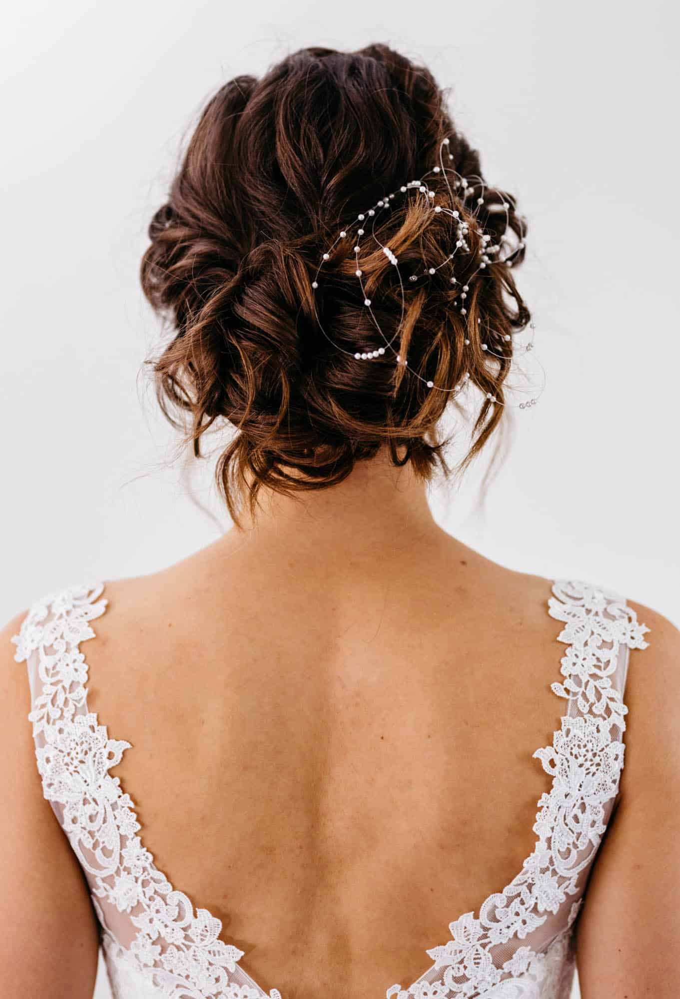     The back view of a woman in a wedding dress with lace and pearls, fitted with beautiful bridal hairstyles.