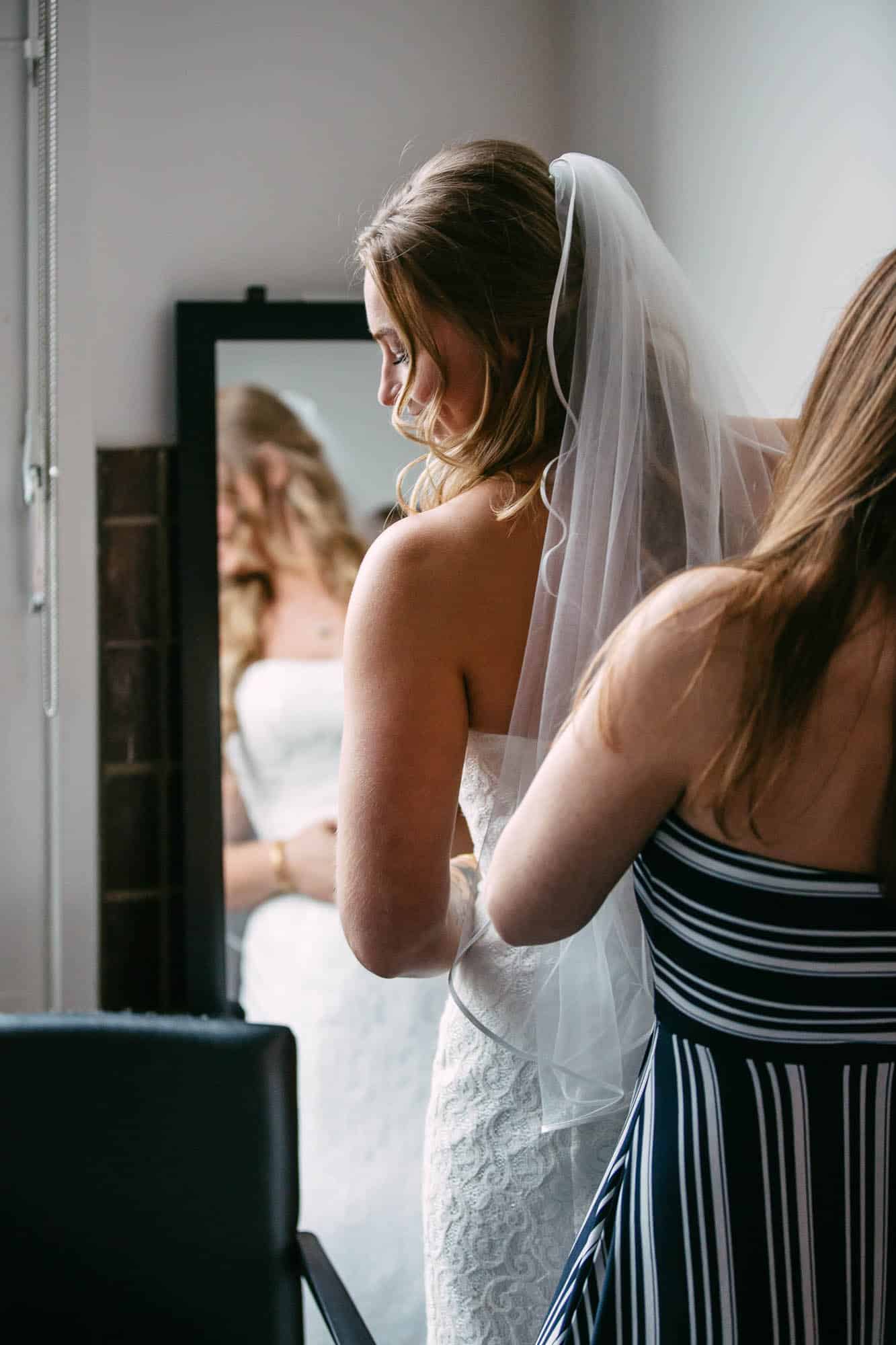 A master of ceremonies helping a bride get ready in front of a mirror.
