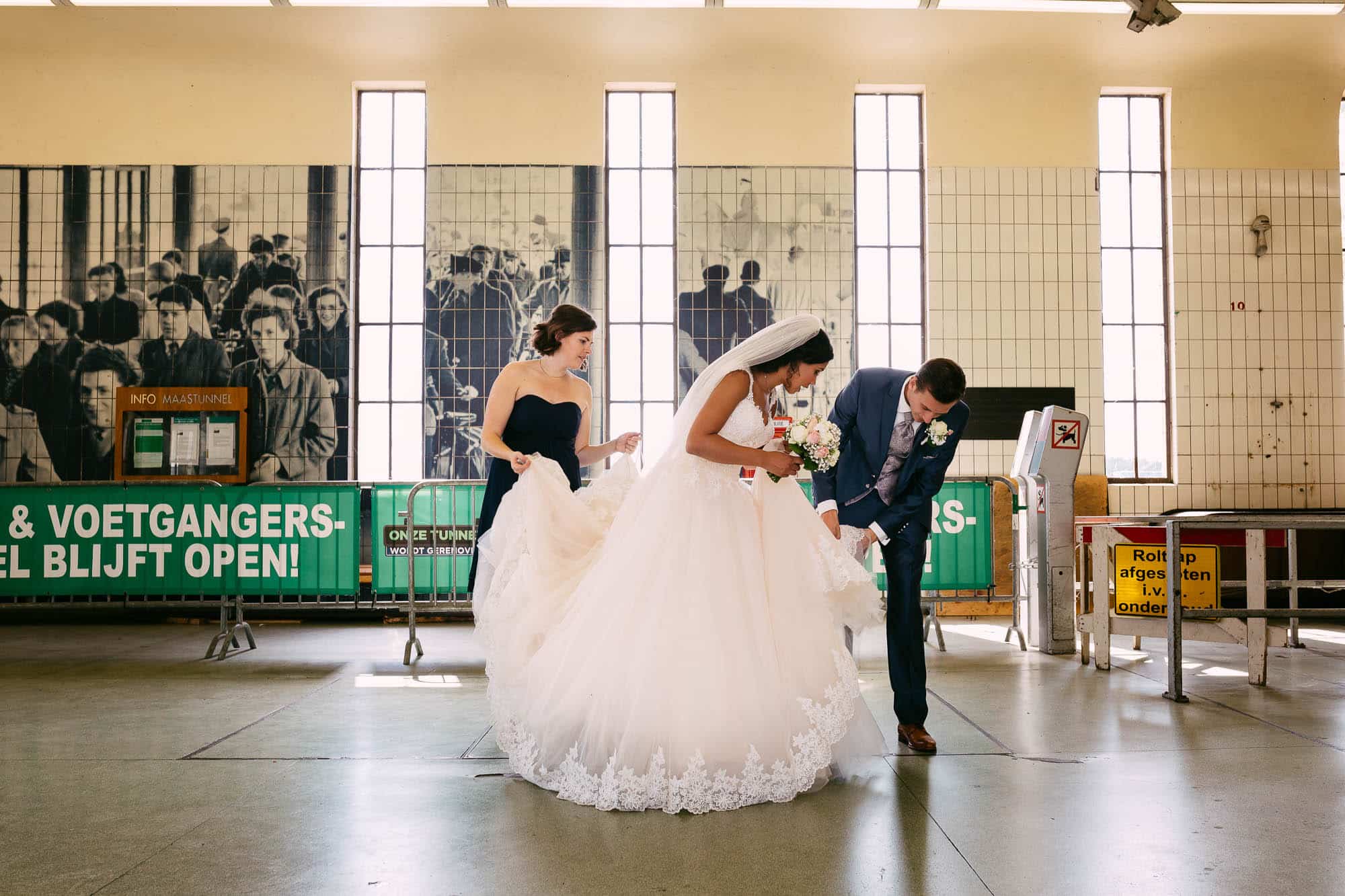 Een bruid en bruidegom lopen, vergezeld van hun ceremoniemeester, door een treinstation.