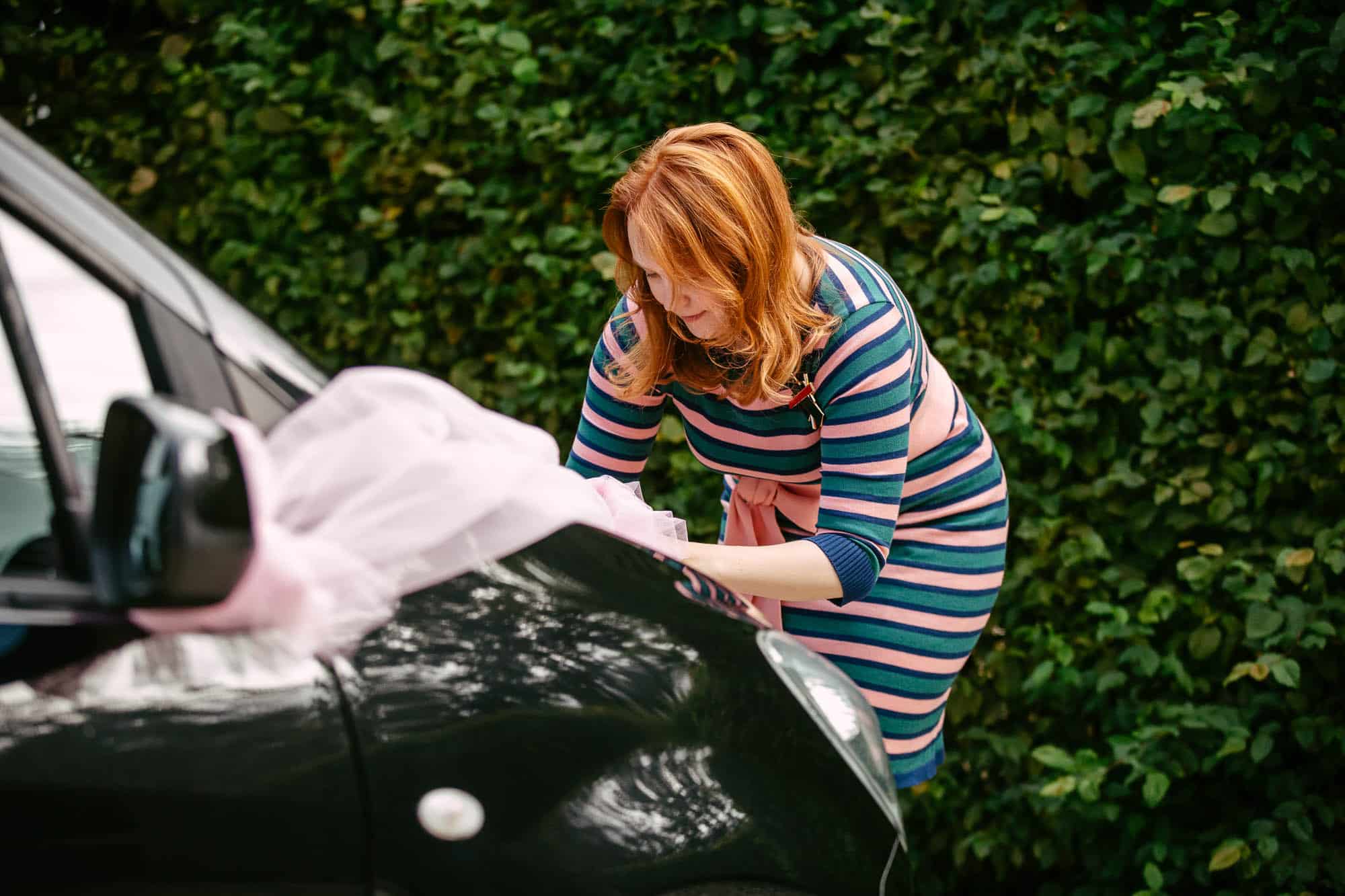 Een vrouw, optredend als ceremoniemeester, plakt roze lint op een zwarte auto.