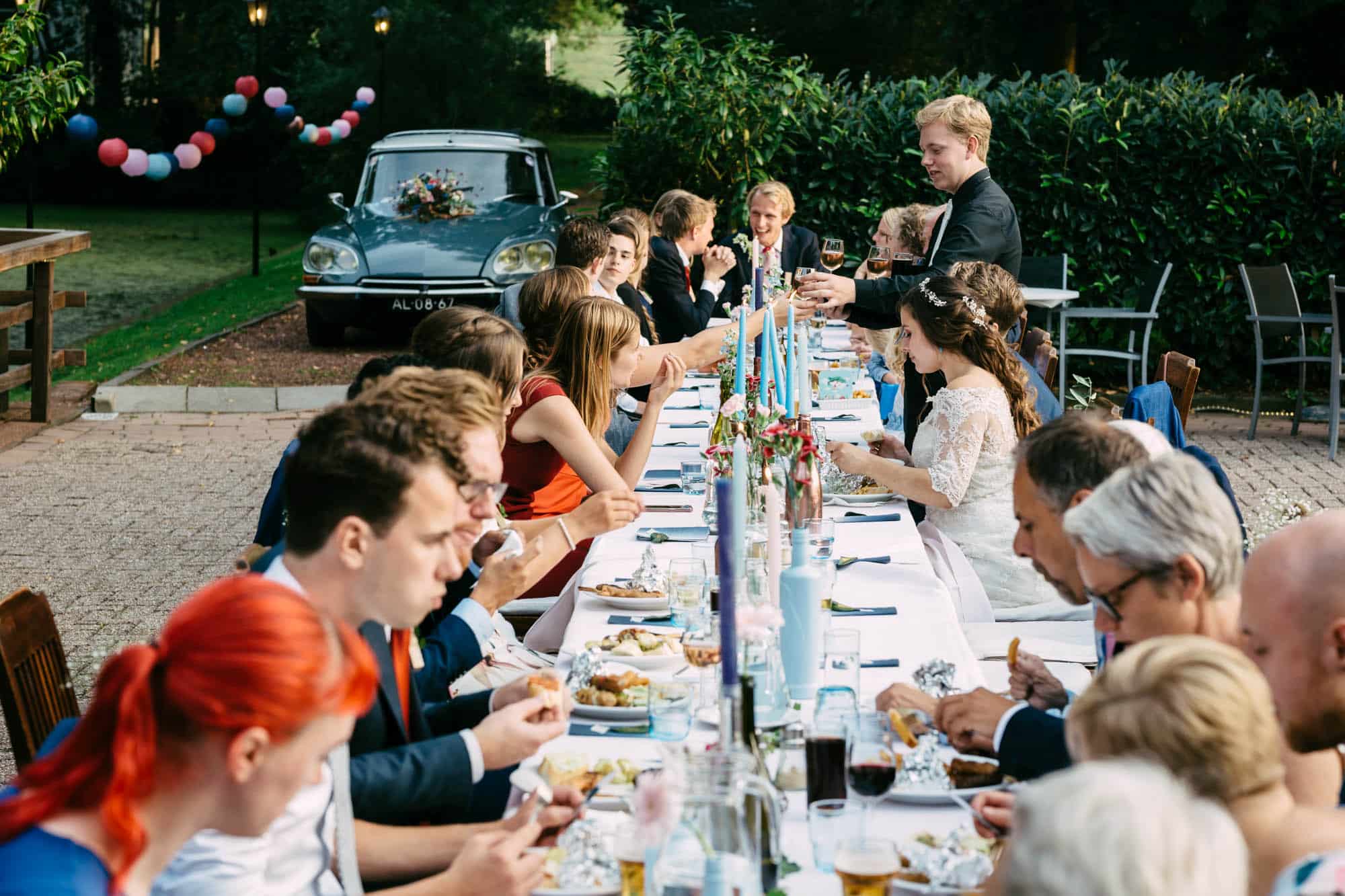 Een groep mensen eet aan een lange tafel in de tuin van het koetshuis rotterdam.