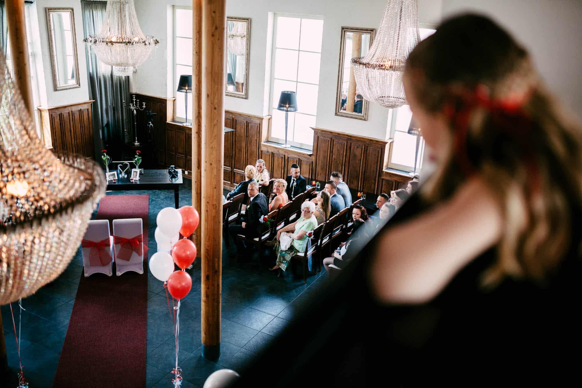 Een huwelijksceremonie in een kamer met kroonluchters en ballonnen.