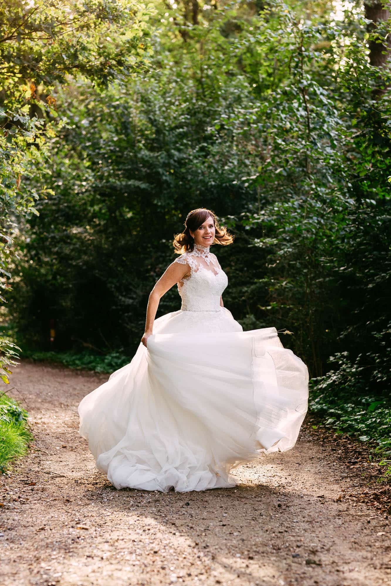 A bride in a beautiful A-line wedding dress runs happily along a forest path.