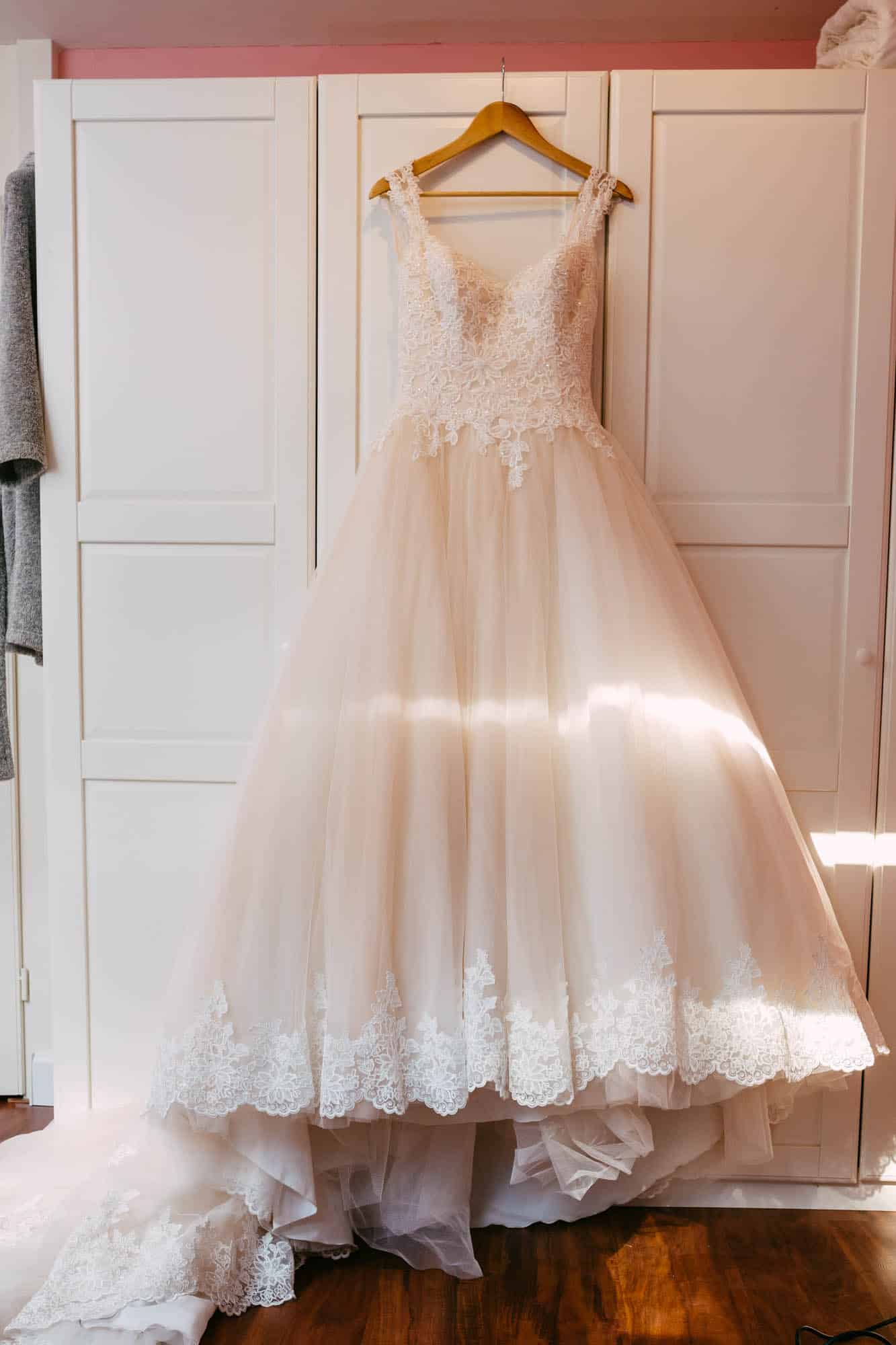 A beautiful A-line wedding dress hangs from a dresser in a beautifully decorated room.