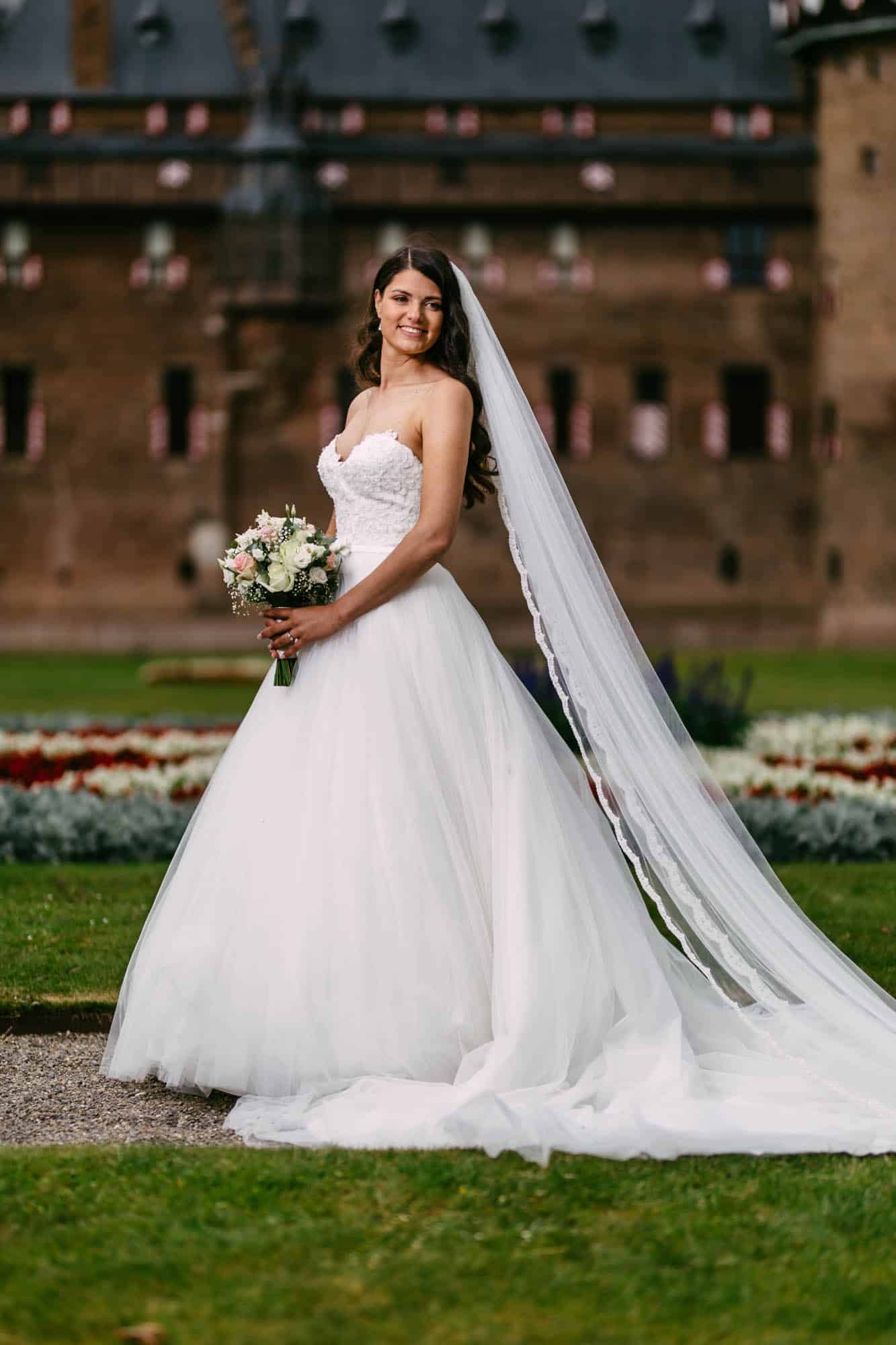 A bride in an A-line wedding dress standing in front of a castle.