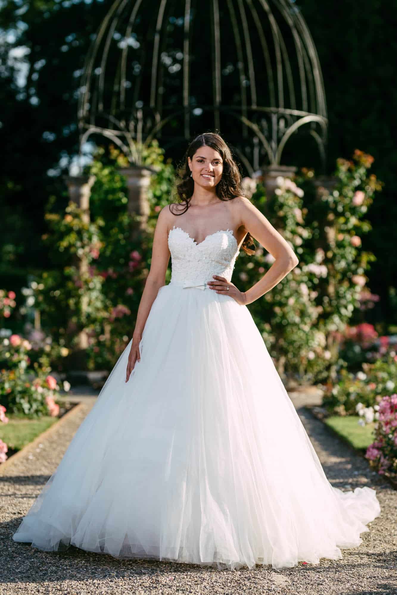 A woman in a wedding dress poses in front of a garden, wearing an elegant A-line gown.
