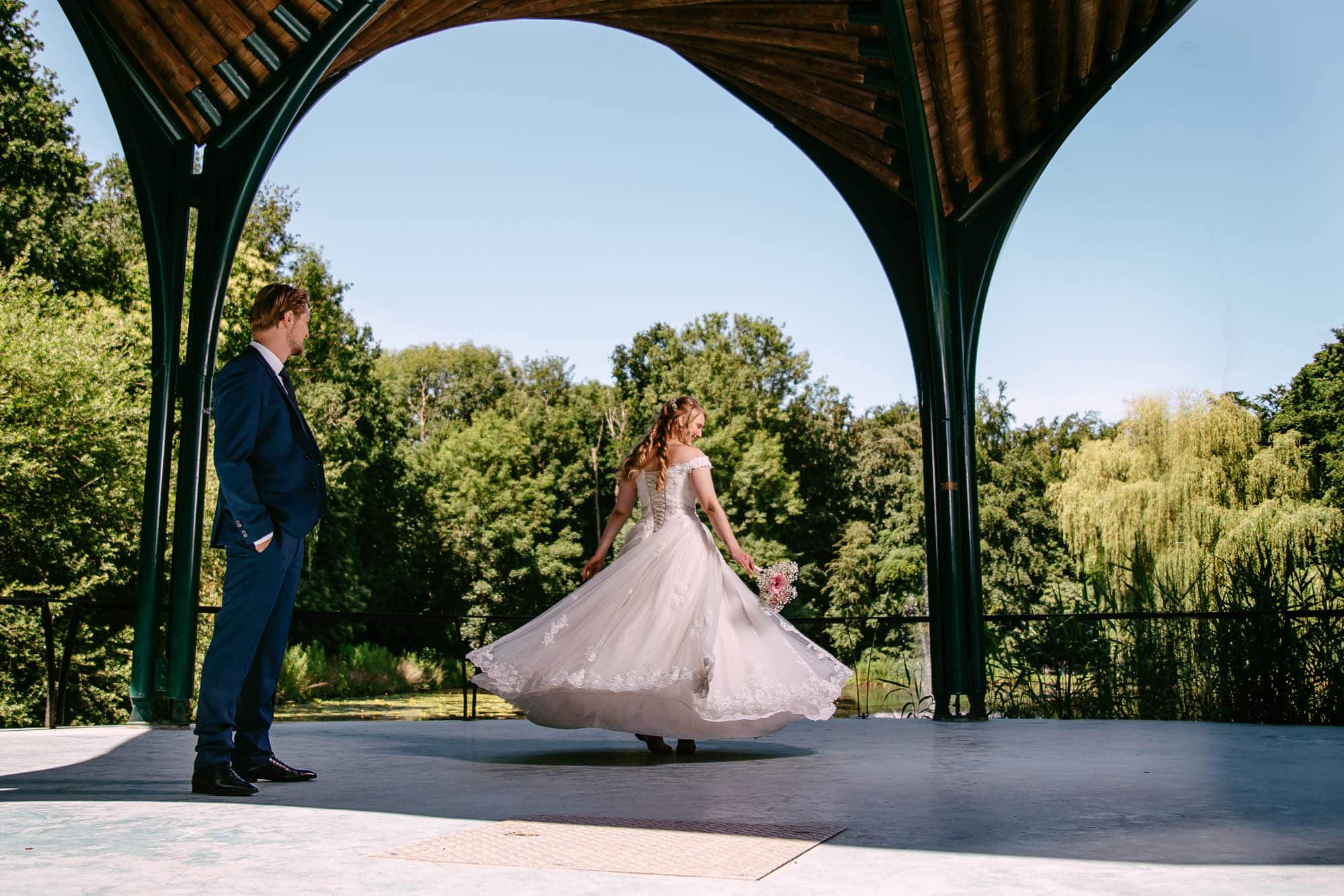 A bride standing under a gazebo in a park, dressed in a beautiful A-line wedding dress, with the groom by her side.
