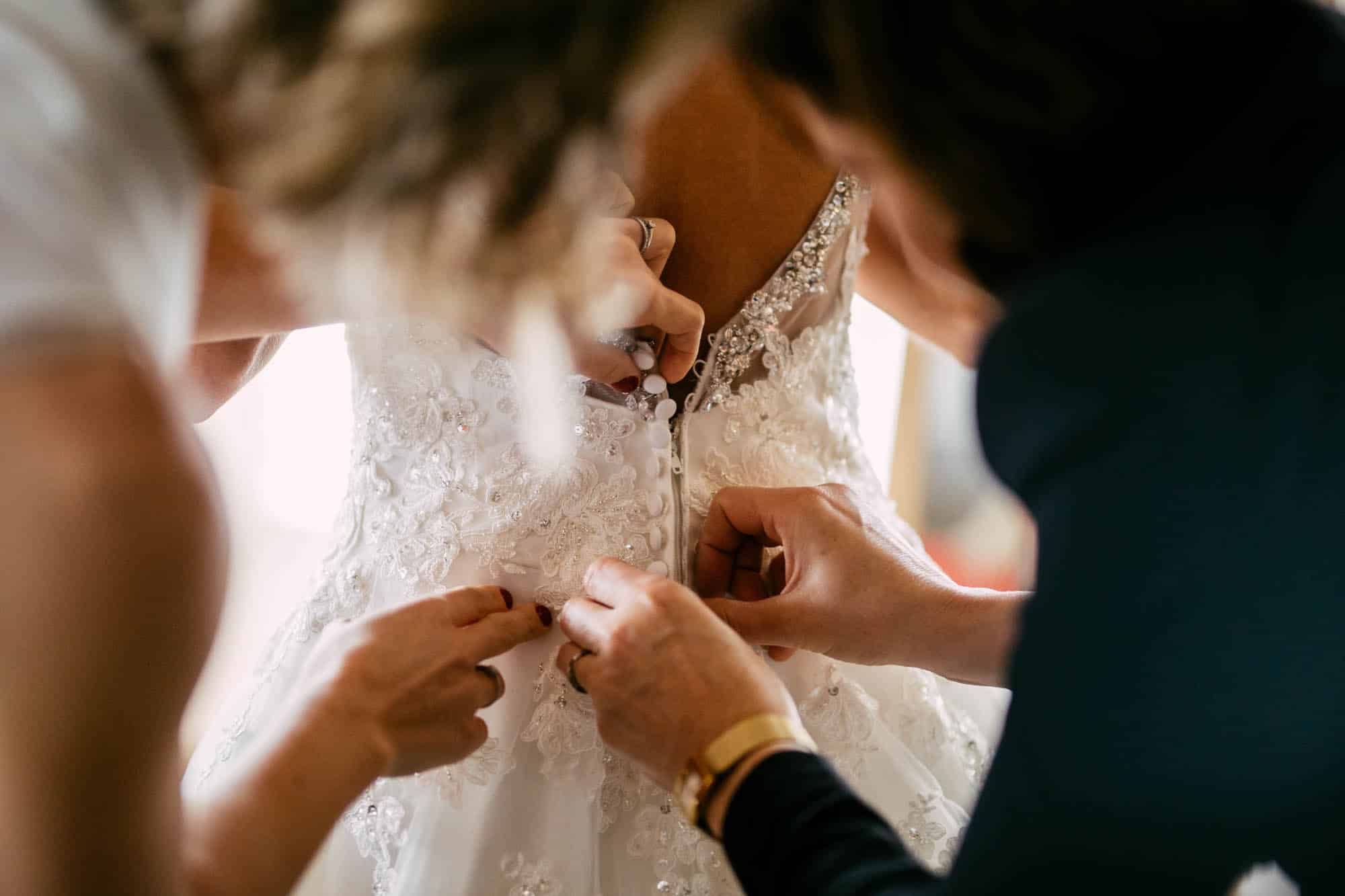A woman carefully attaches a button to an A-line wedding dress.