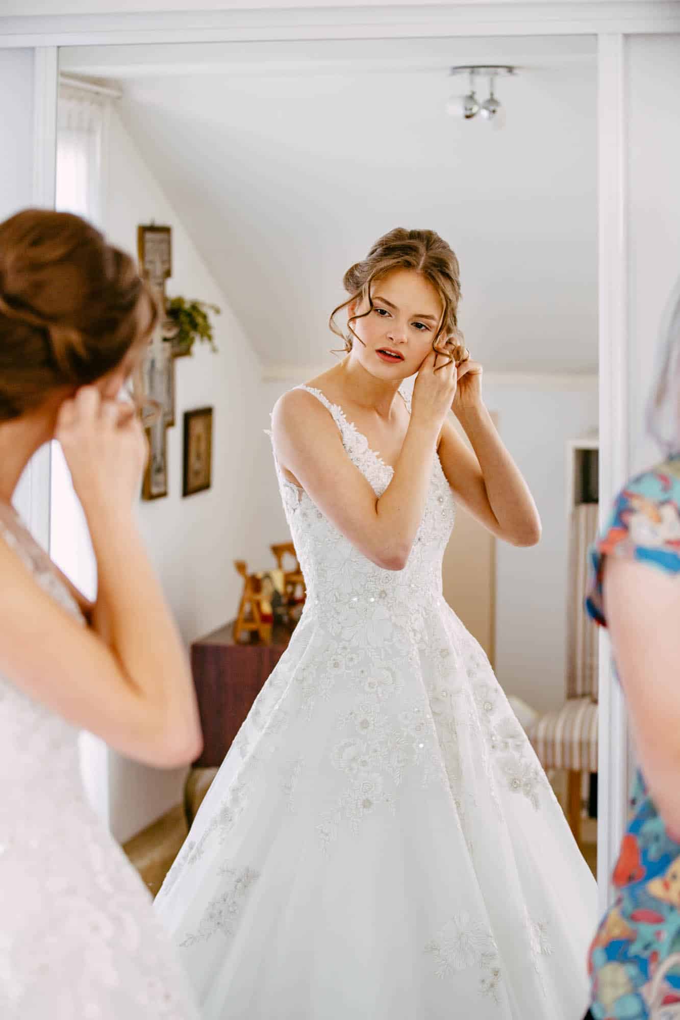A bride puts on her A-line wedding dress in front of a mirror.