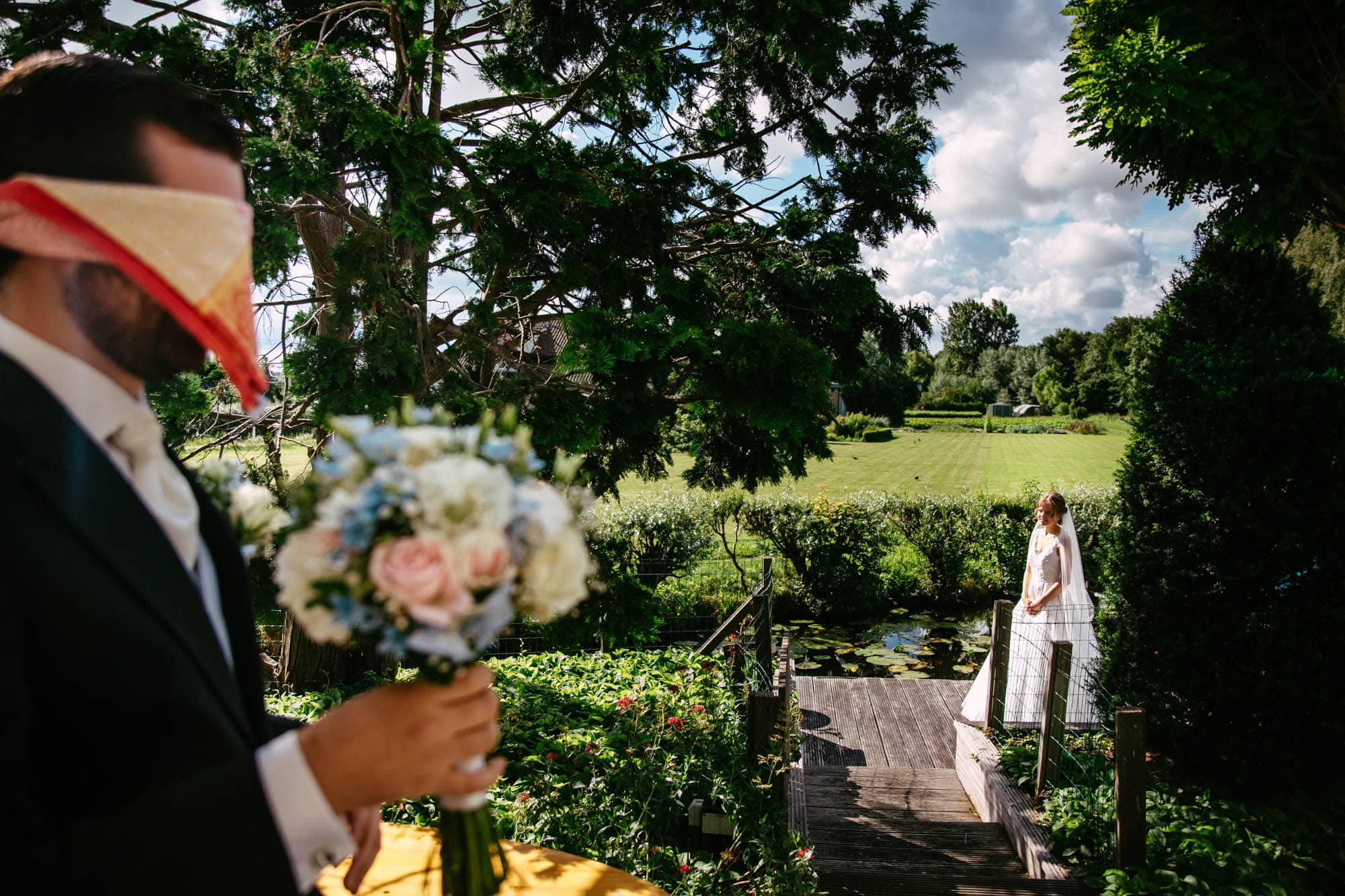 A bride and groom in an elegant A-line wedding dress holding a veil in front of a beautiful garden.