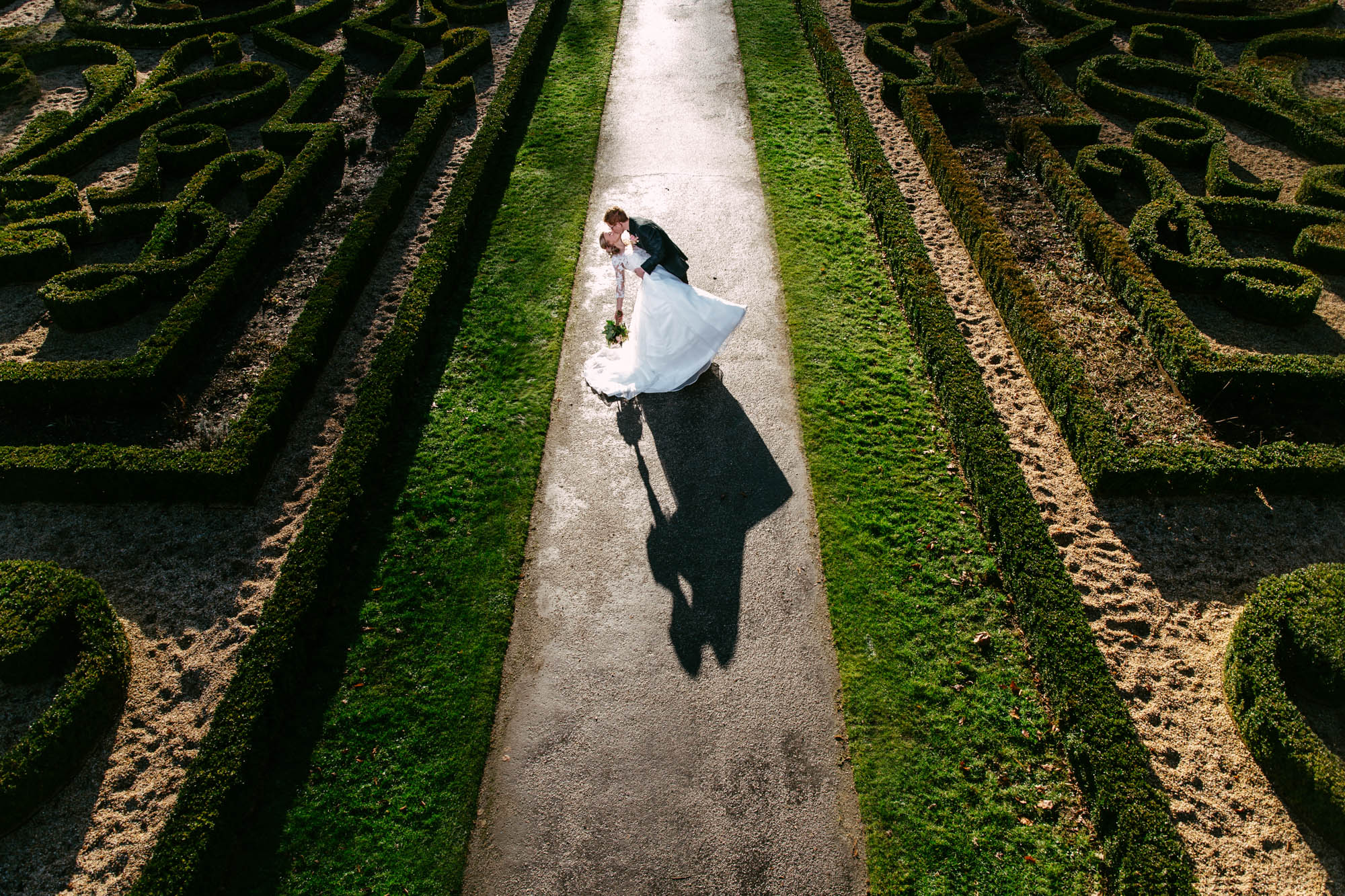 A bride in an A-line wedding dress and groom walk through a maze.