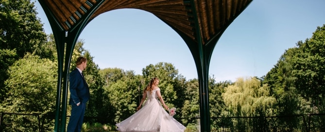 A bride and groom stand under a gazebo, the bride wearing a beautiful A-line wedding dress.