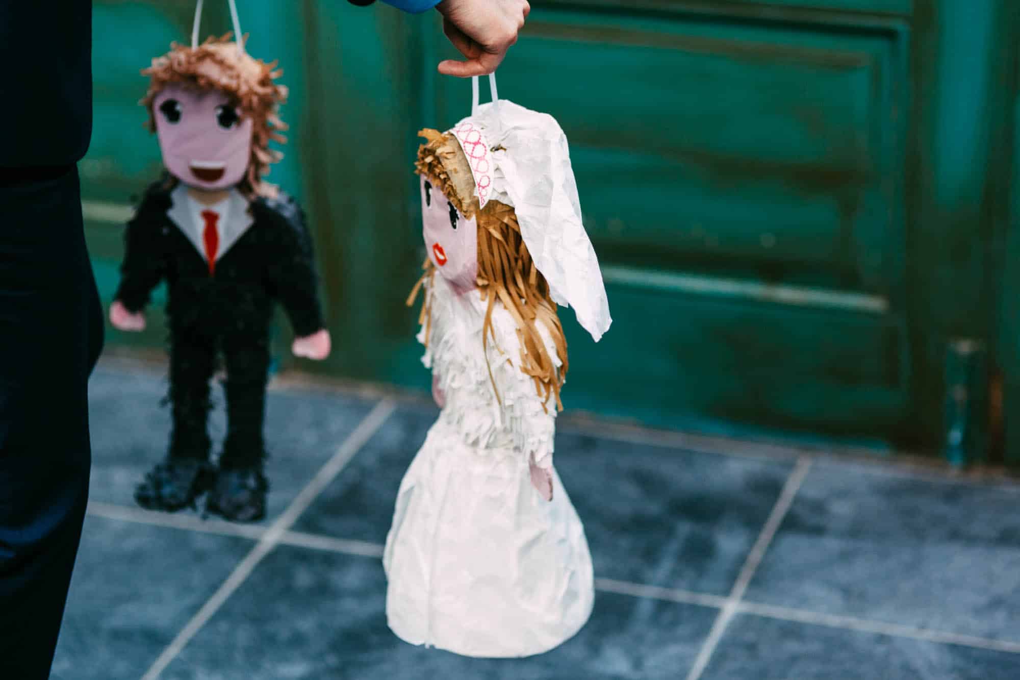 A man plays a marriage game and holds two dolls in front of a door.