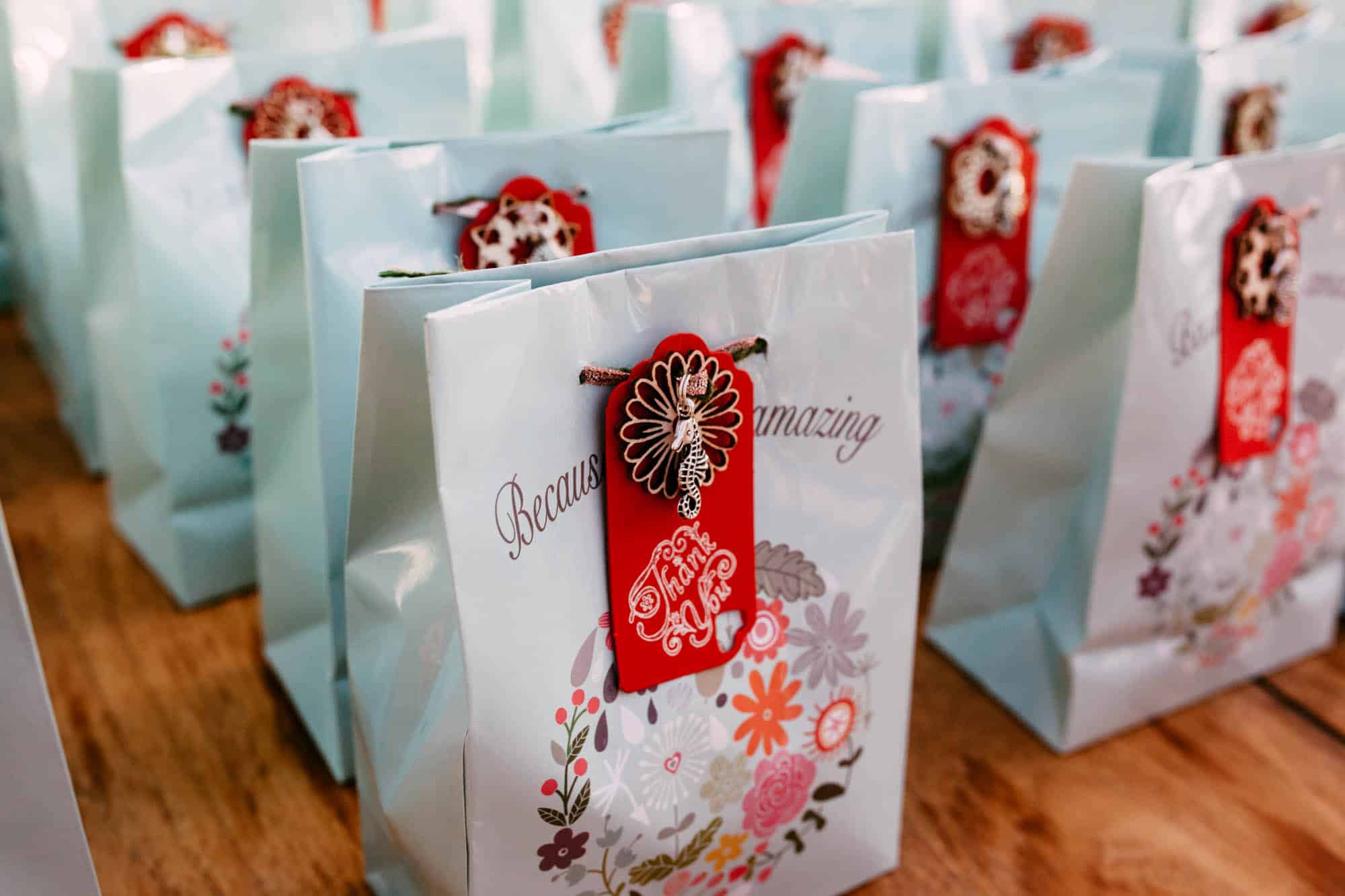 A row of gift bags with red and white ribbons, perfect for a wedding day gift.