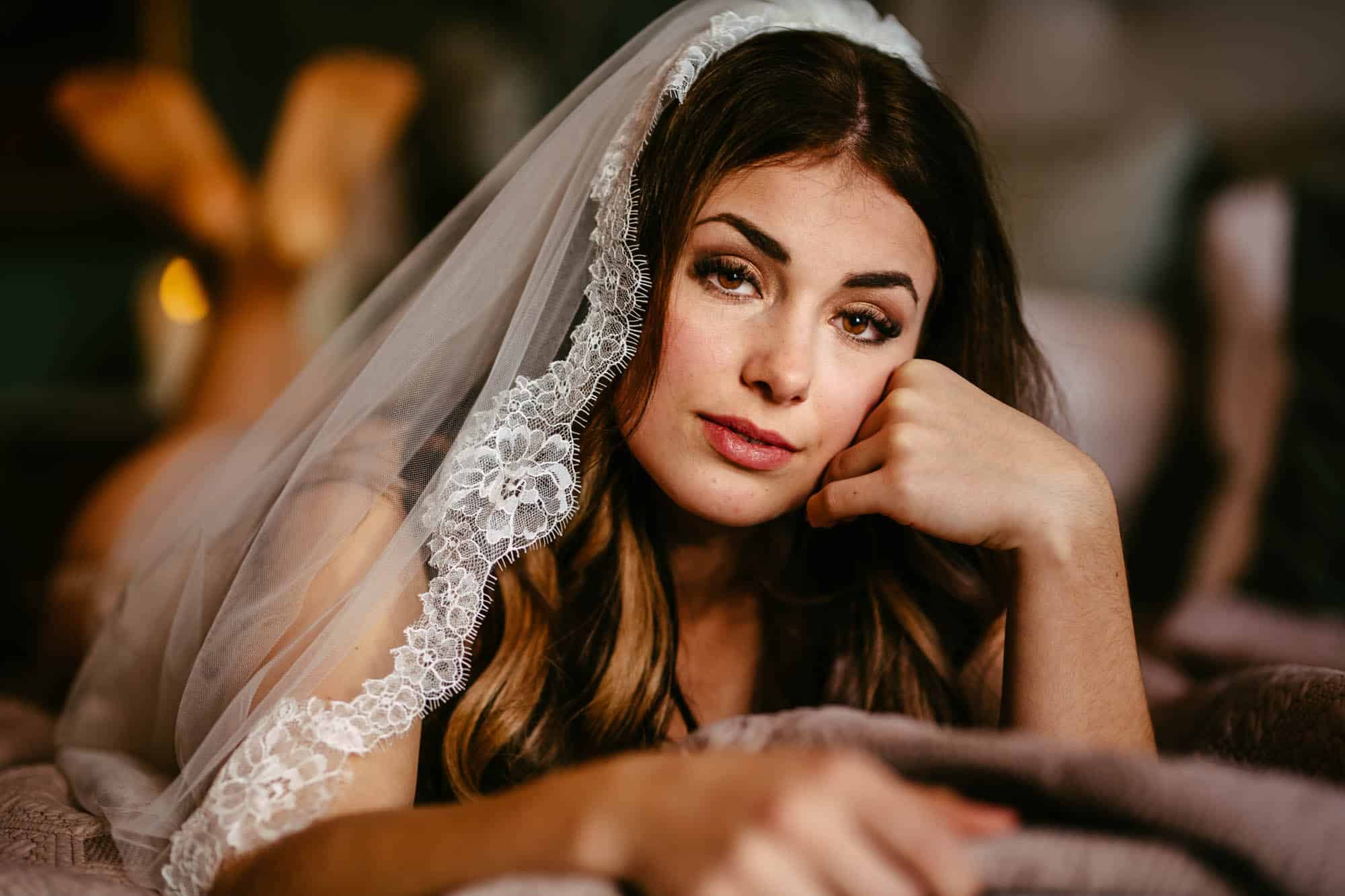 A beautiful woman lying on a bed, dressed in bridal lingerie and a veil.