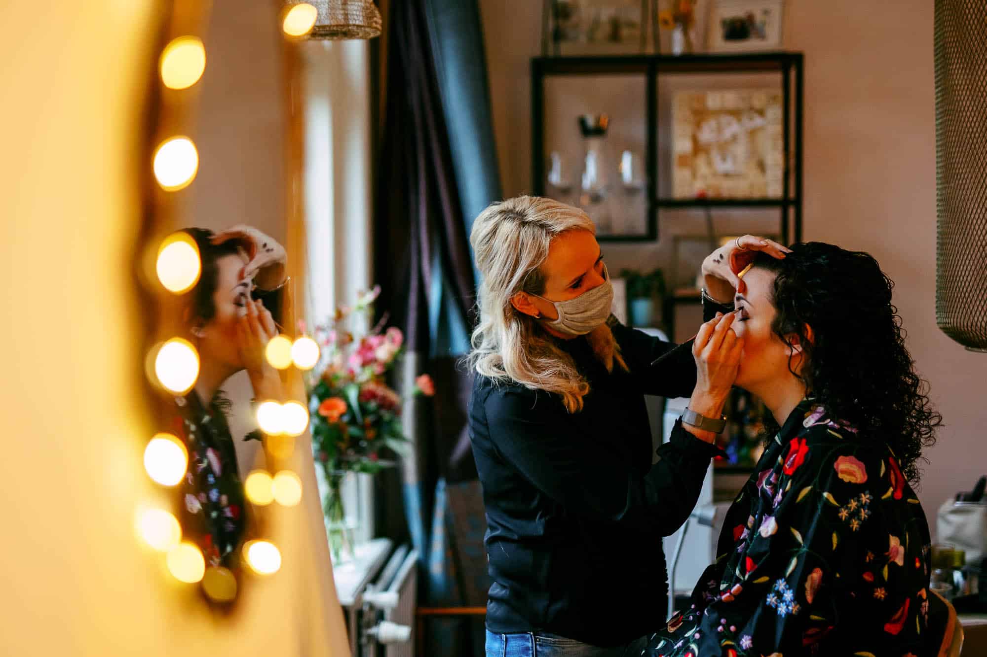 A woman having her bridal make-up done in front of the mirror.