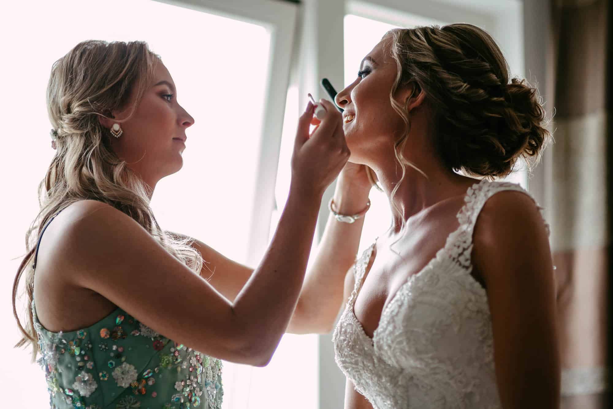 A bridesmaid expertly applies bridal make-up on the bride.
