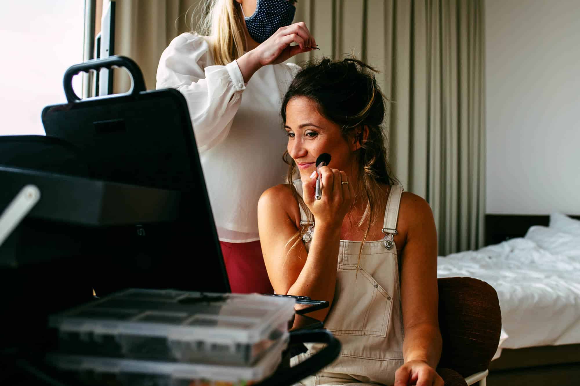 Een vrouw laat haar bruidsmake-up doen in een hotelkamer.