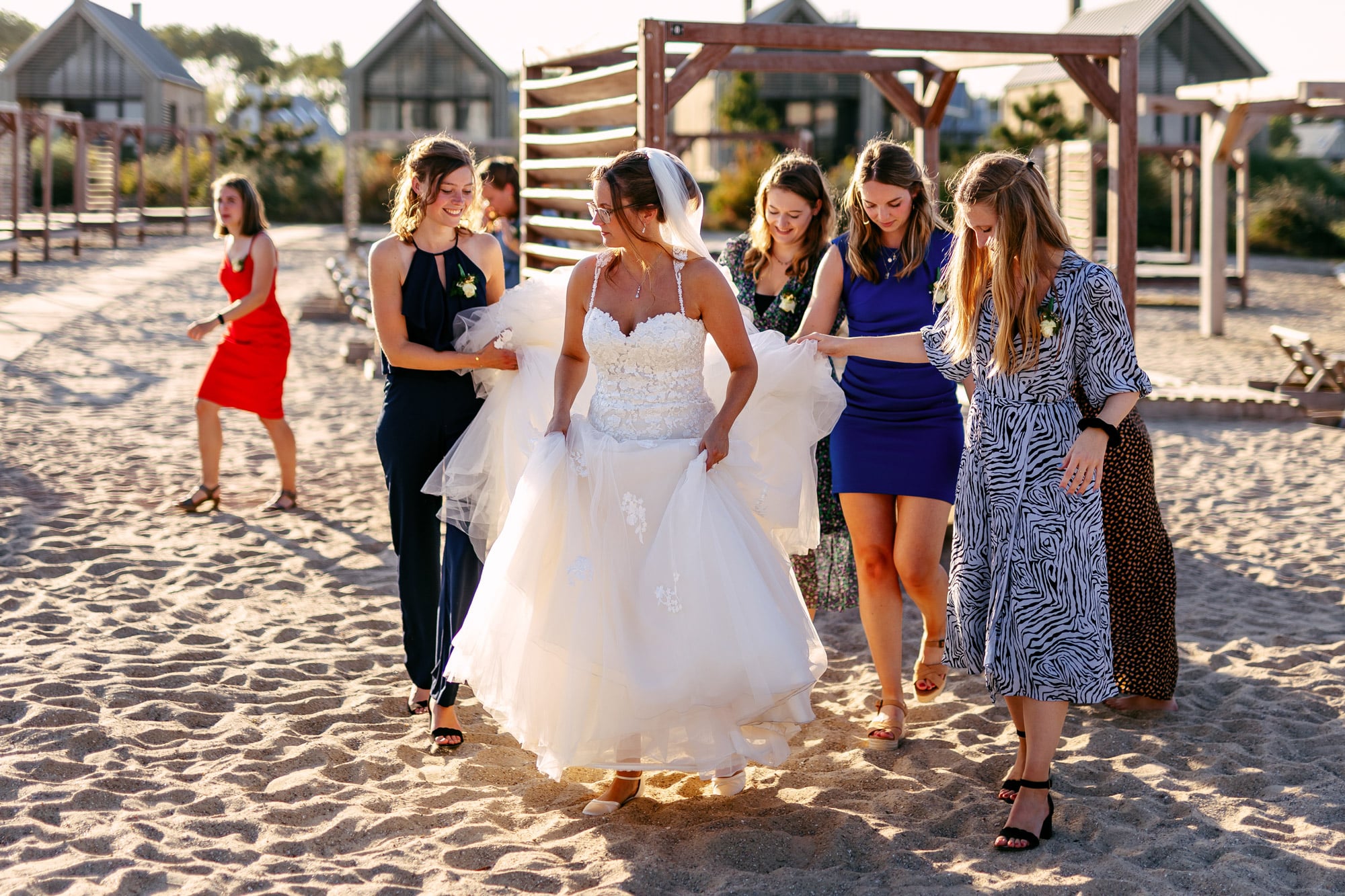 A wedding day bride and her bridesmaids walk on the beach.