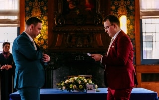 Twee mannen in pak met een bruiloftsthema kijken elkaar aan een tafel aan.