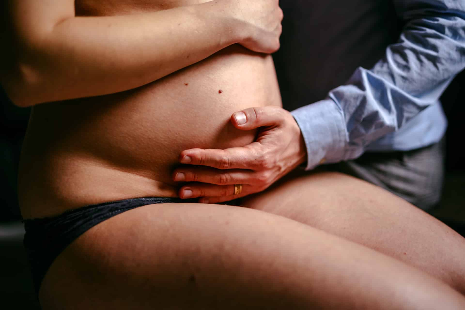 Tijdens een Zwangerschapsshoot raakt een man zachtjes de buik van de zwangere vrouw aan.