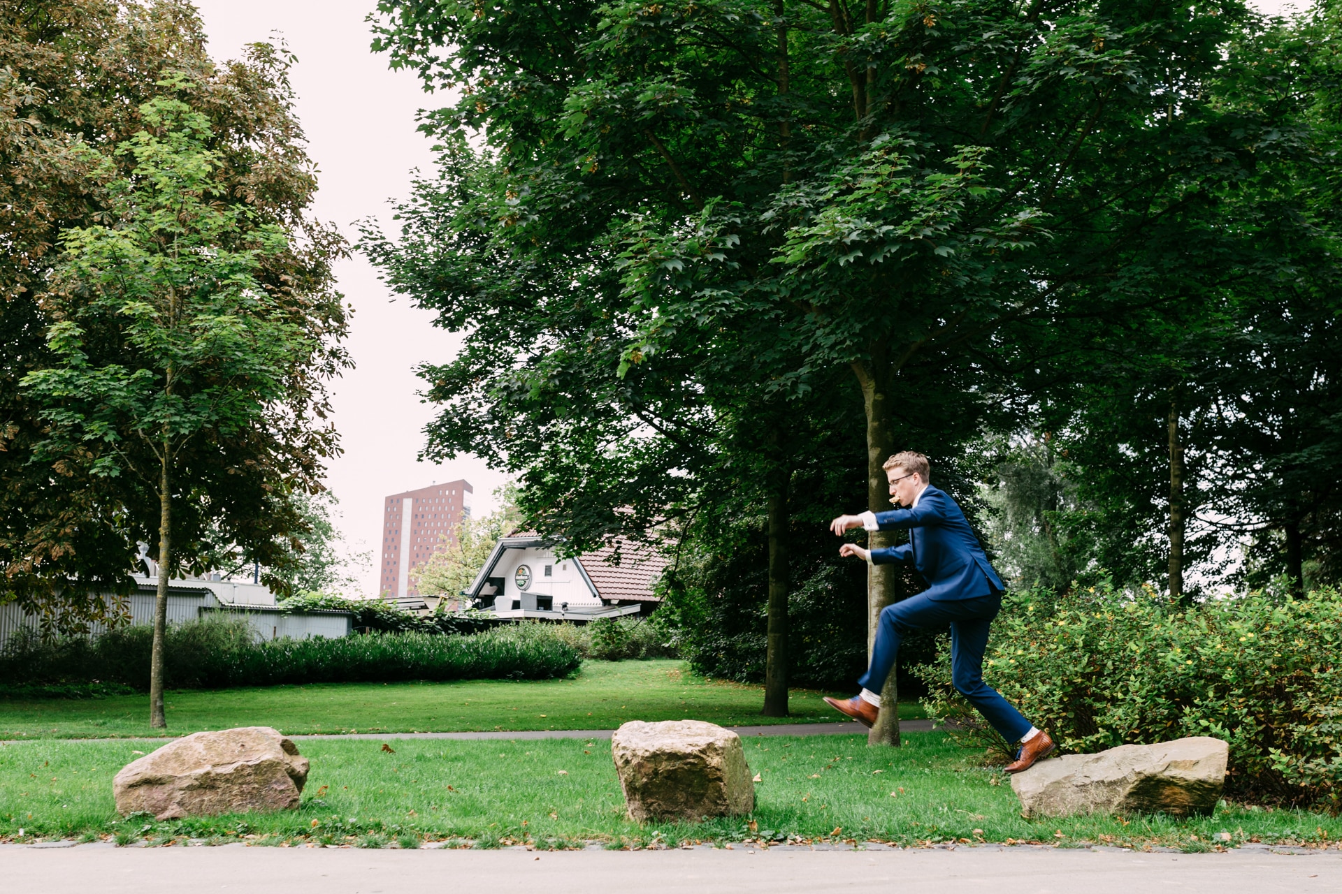 A man in a suit jumps over rocks in a park during Weddings in the Woods.
